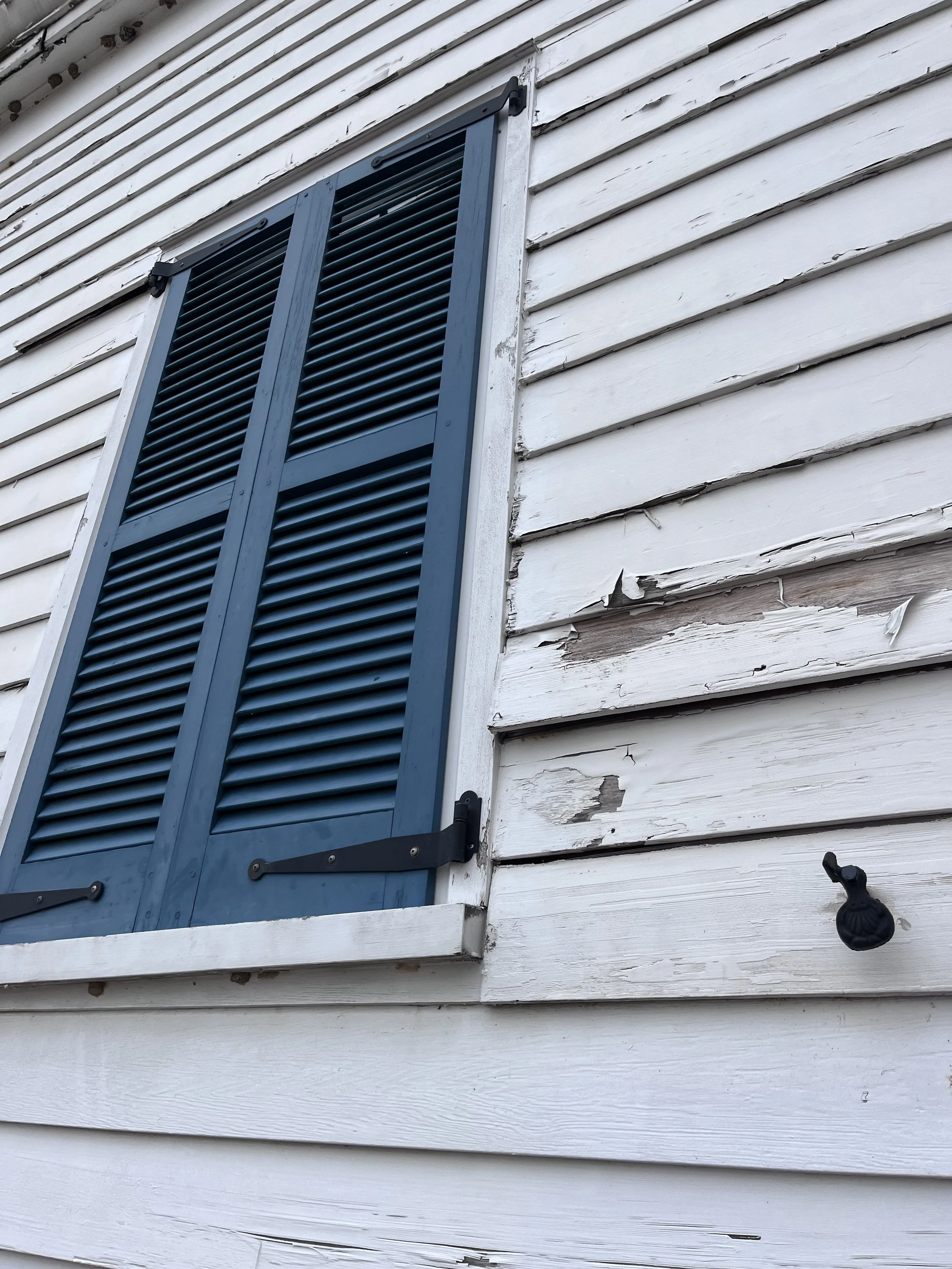 Close-up of blue wooden shutters and peeling white paint on the exterior of the historic keeper’s house at Jones Point Lighthouse.
