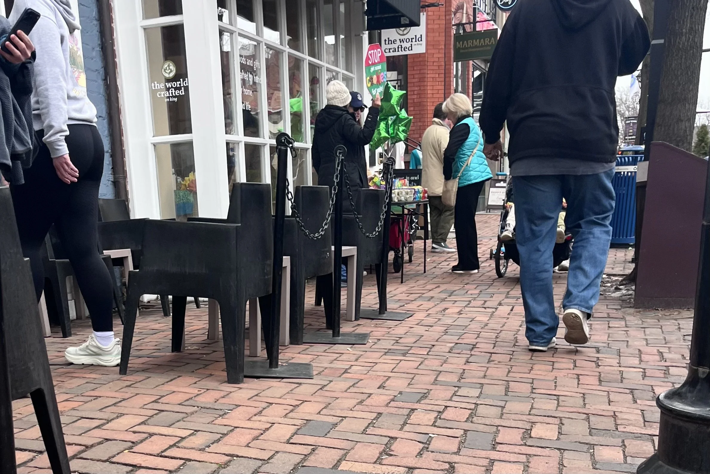 Narrow brick sidewalk on King Street in Old Town Alexandria with outdoor dining chairs, pedestrians, and limited space to pass comfortably with a small dog.