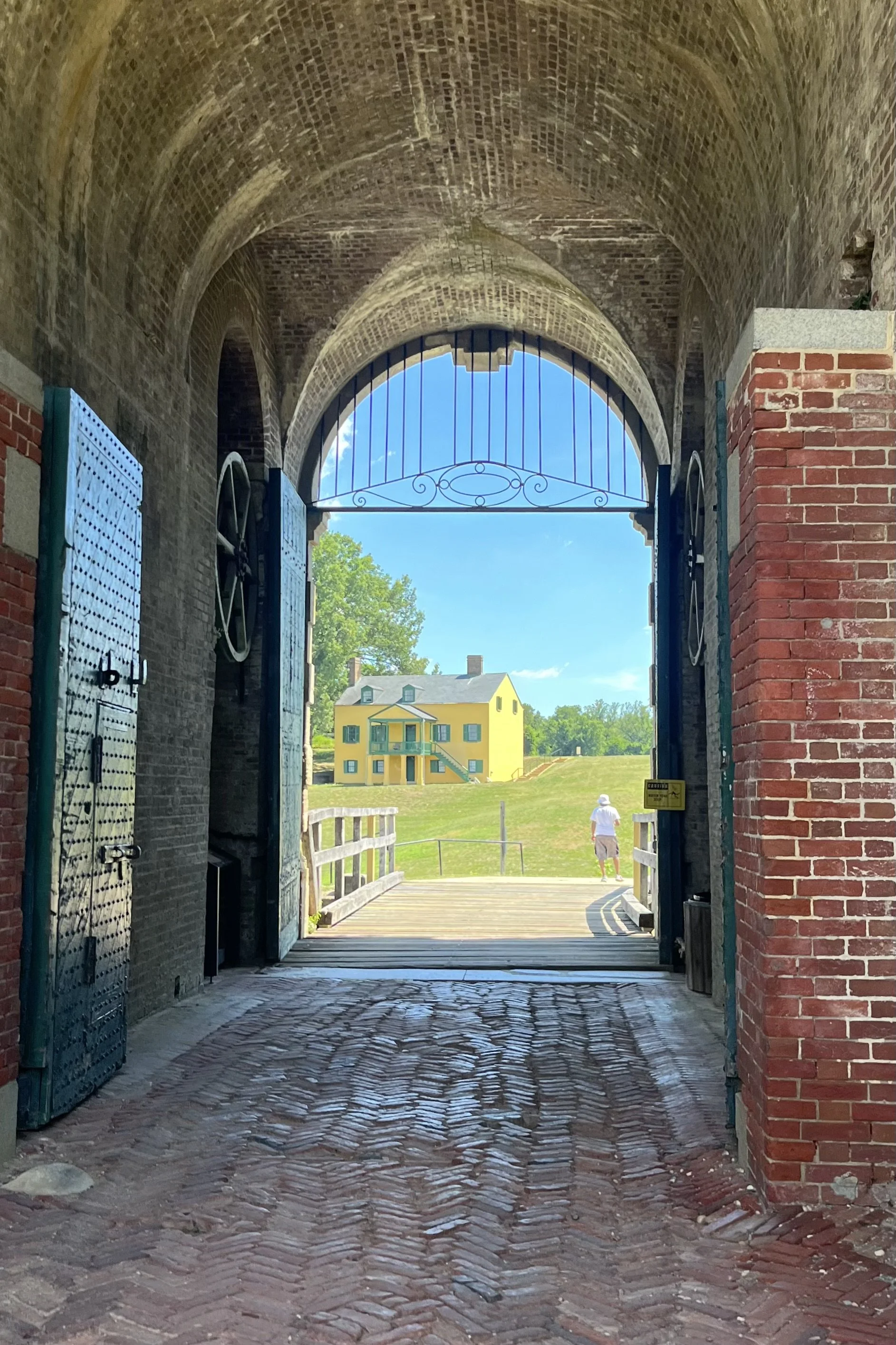 Brick-vaulted archway inside Fort Washington Park framing a yellow historic building and grassy courtyard beyond.