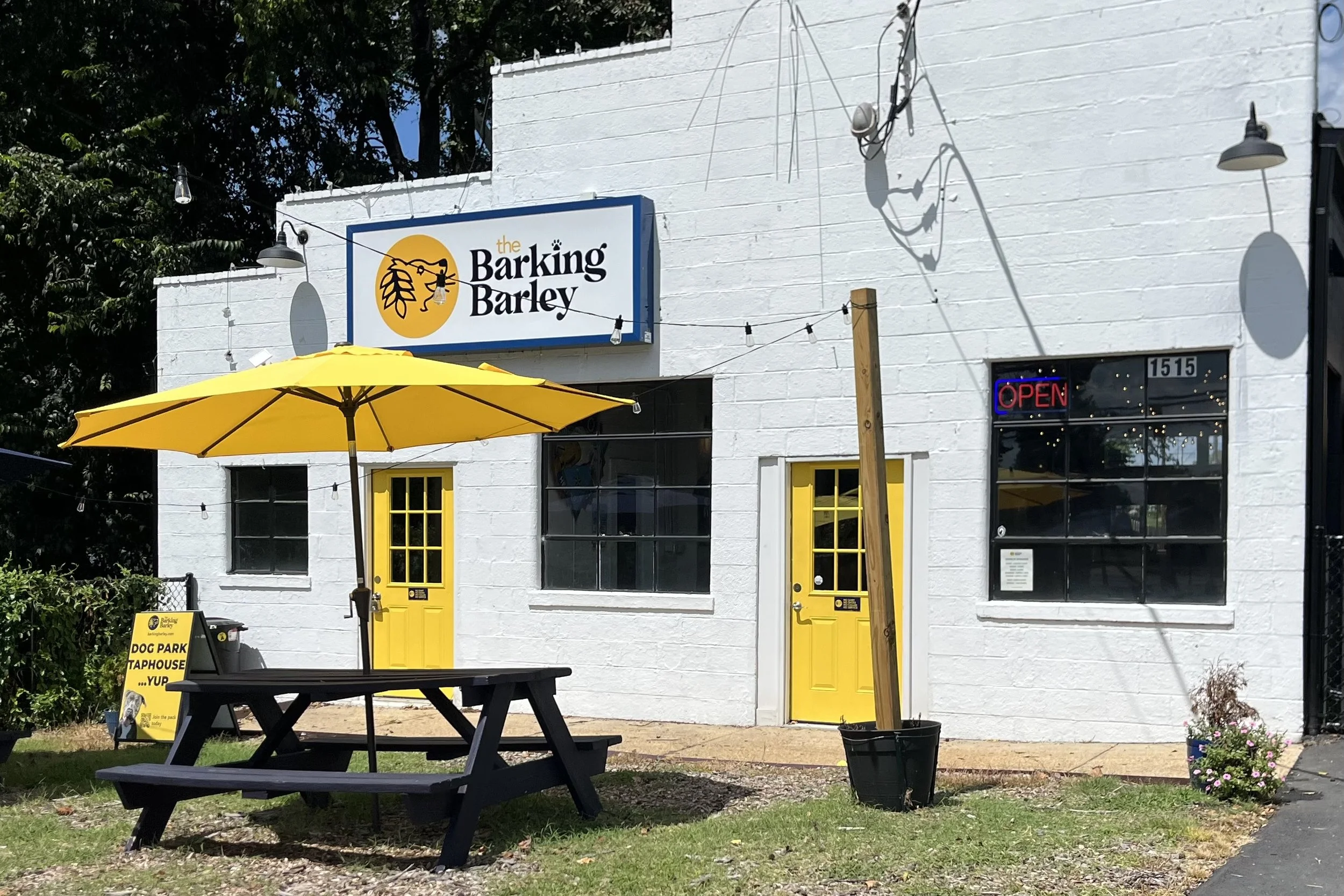 The Barking Barley exterior in Fredericksburg with yellow doors, a yellow patio umbrella and a sign advertising its dog park and taphouse.