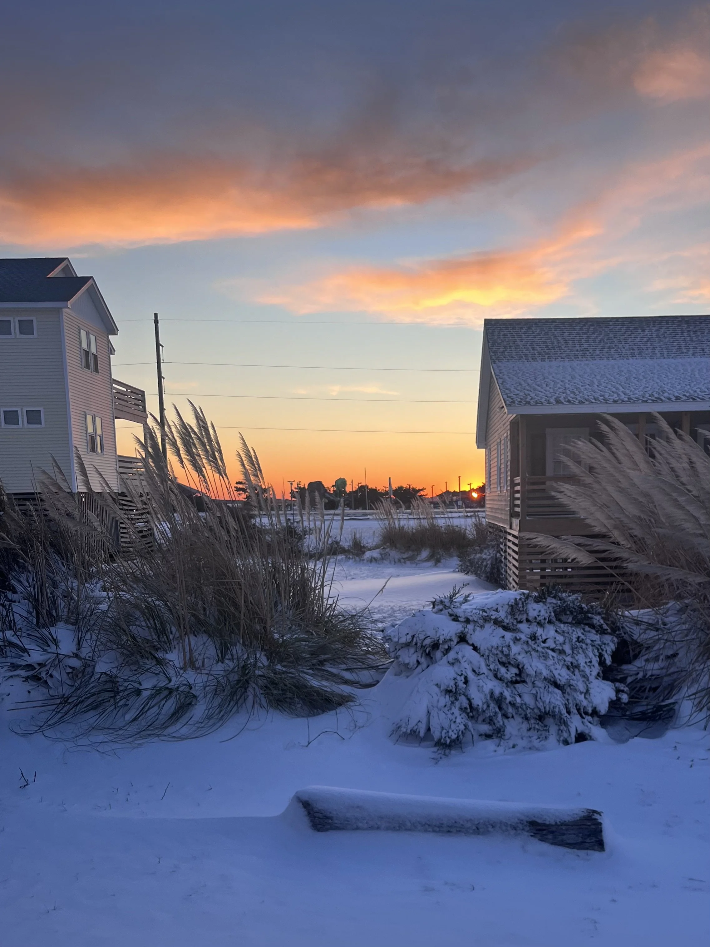 Snow-covered coastal homes and dunes at sunrise after a winter storm in the Outer Banks.