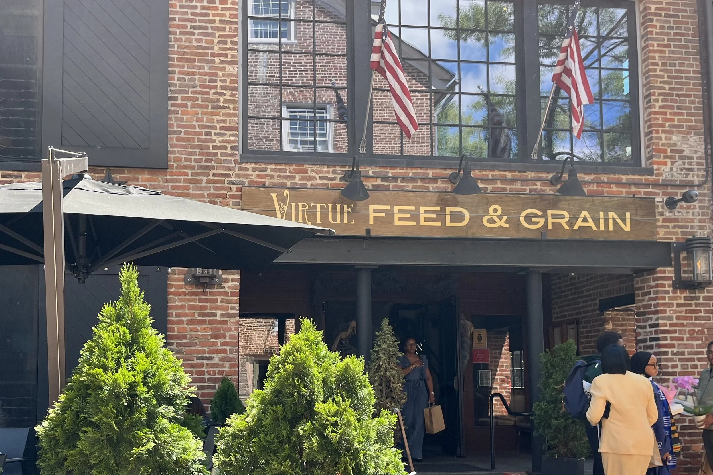 Exterior of Virtue Feed & Grain in Old Town Alexandria with brick architecture, outdoor patio umbrellas, and entrance along Wales Alley.