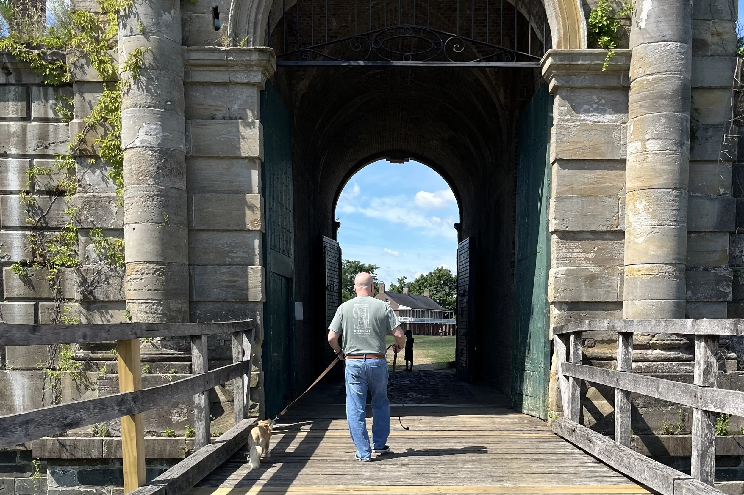 Visitor and small dog crossing the wooden bridge and entering the historic stone gate at Fort Washington.