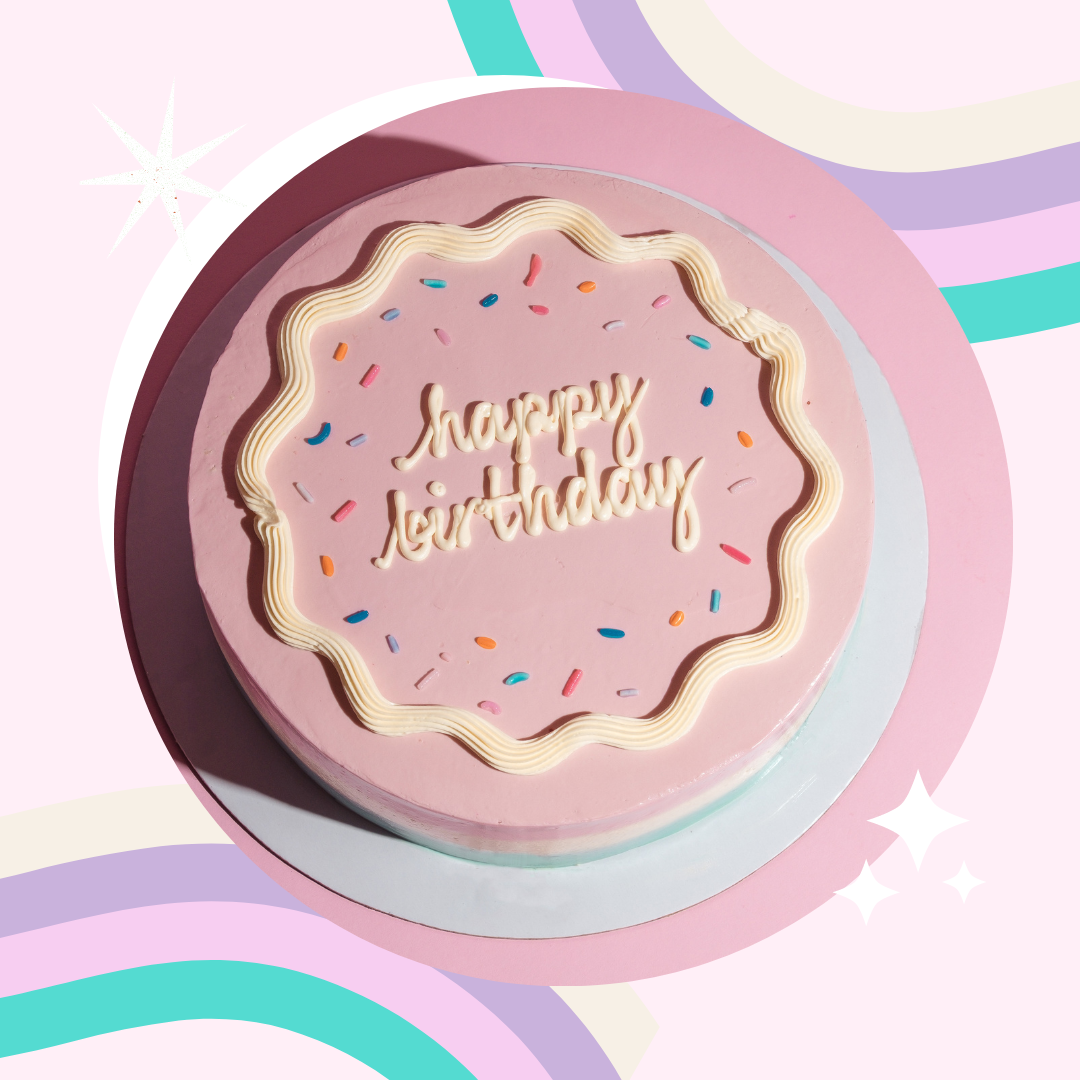 Pink birthday cake with a white icing border and colorful sprinkles, with "happy birthday" written in white icing on top, placed on a pastel rainbow-colored background.