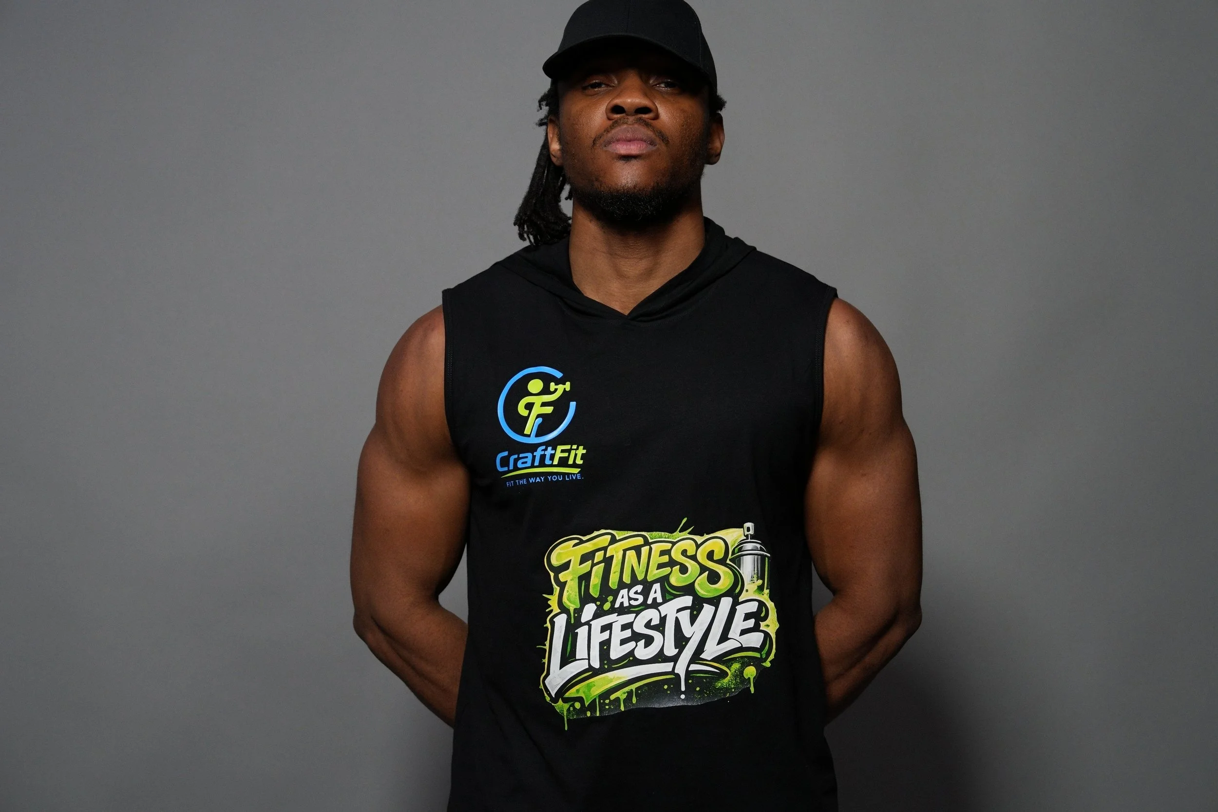 A man wearing a black tank top with fitness-themed graphics and text, including phrases like "CraftFit" and "Fitness as a Lifestyle," standing in front of a plain gray background.
