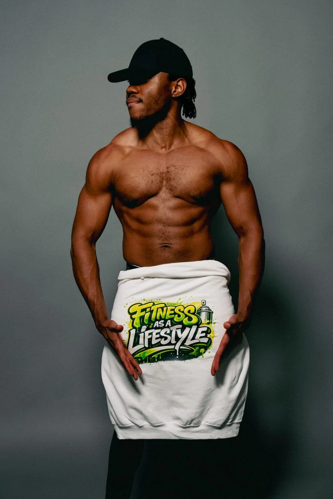 A shirtless man wearing a black cap and a white cloth with a graphic that reads 'Fitness as a Lifestyle,' standing against a plain gray background.