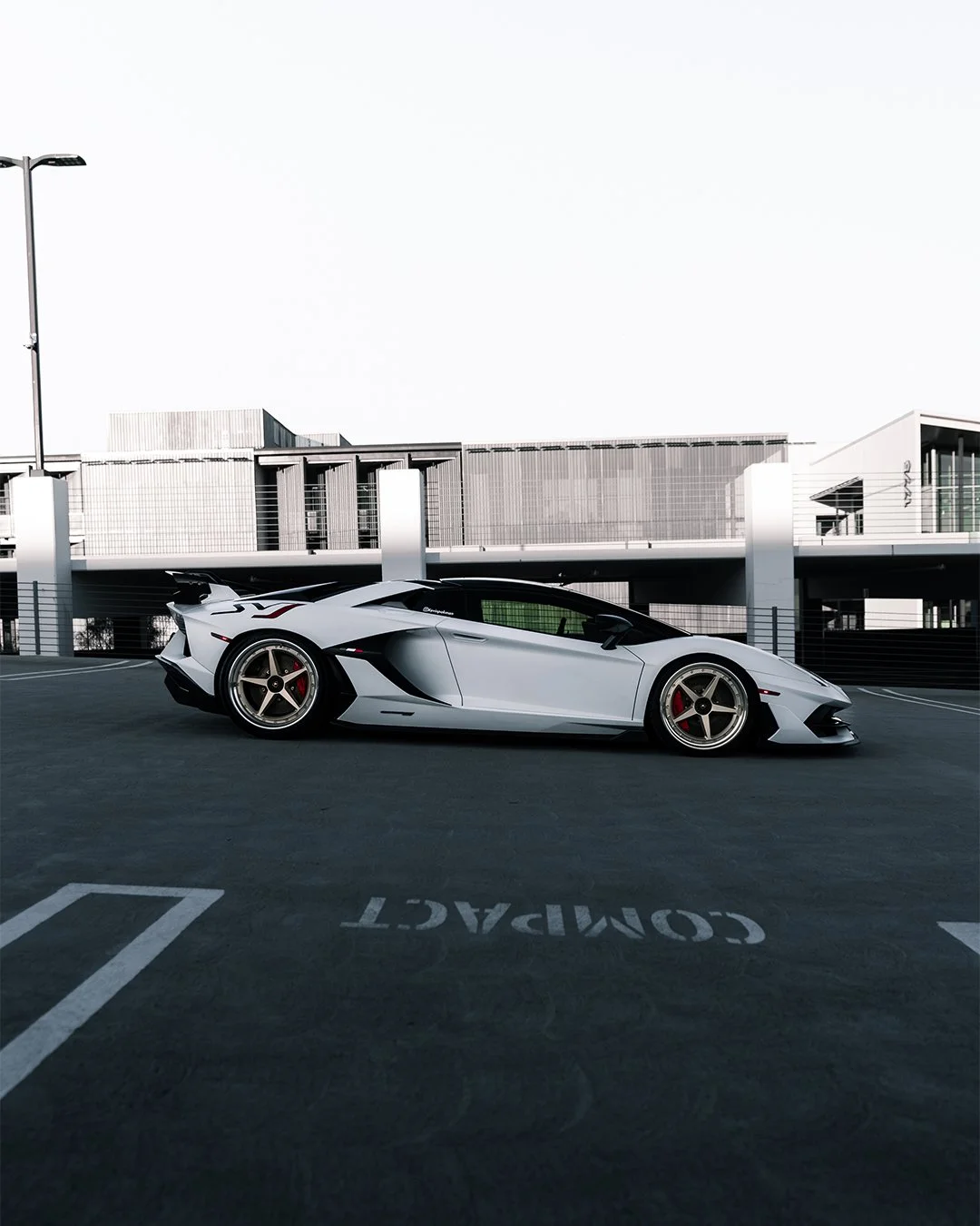 A white Lamborghini sports car parked in a parking lot with a modern building in the background.