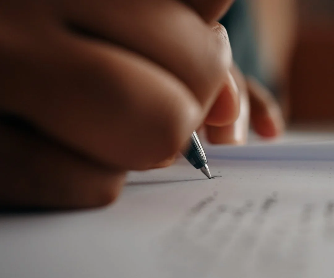 A person's hand holding a silver pen, writing on a white sheet of paper.
