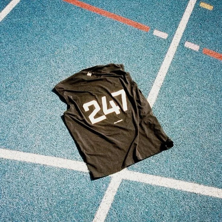 A black sports jersey with the number 247 lying on a blue running track with white lines.