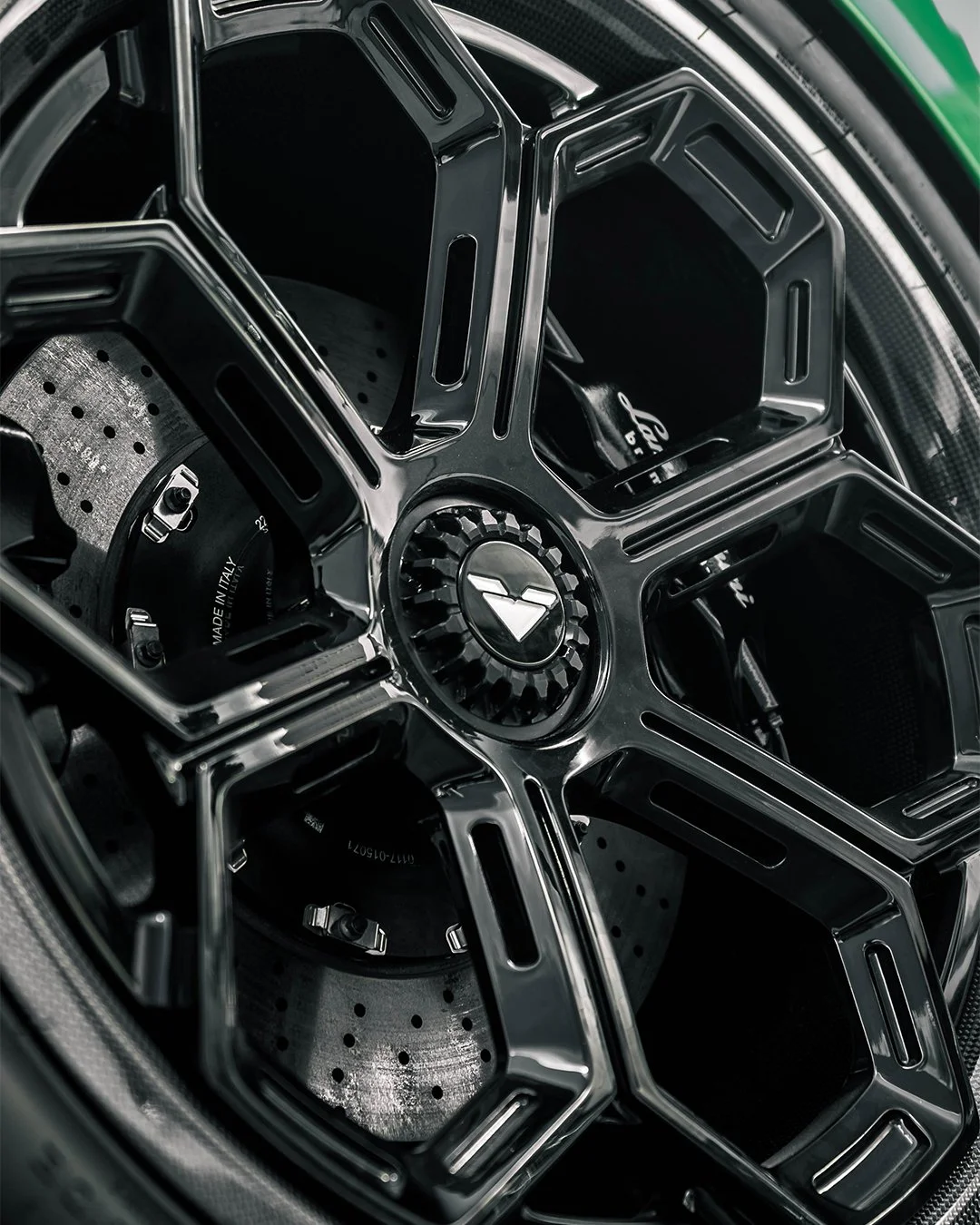 Close-up of a black car wheel with a detailed rim and a central hub featuring a logo, showcasing the brake disc and caliper behind the rim.