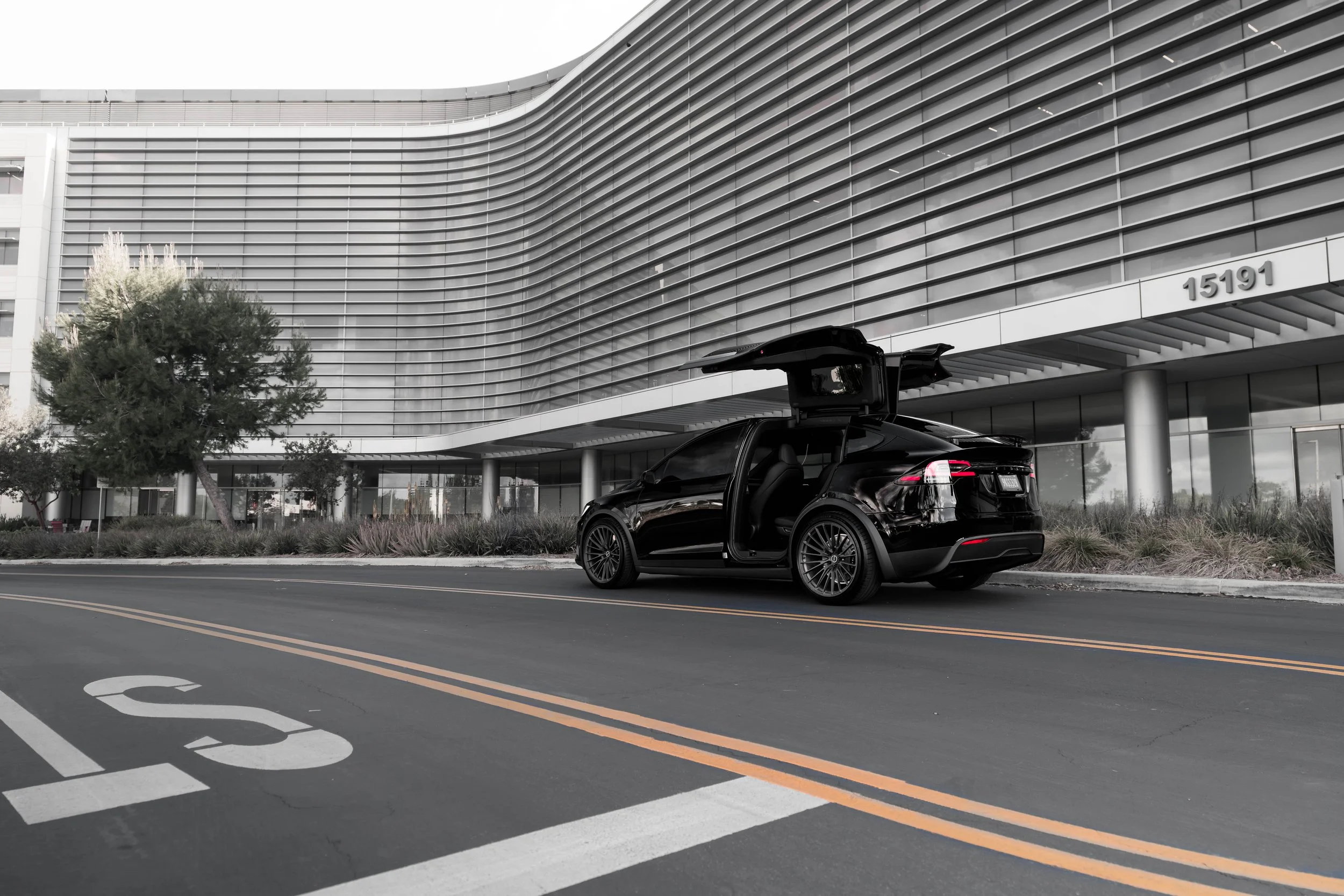 A black car with its gullwing doors open parked on the street in front of a modern building.