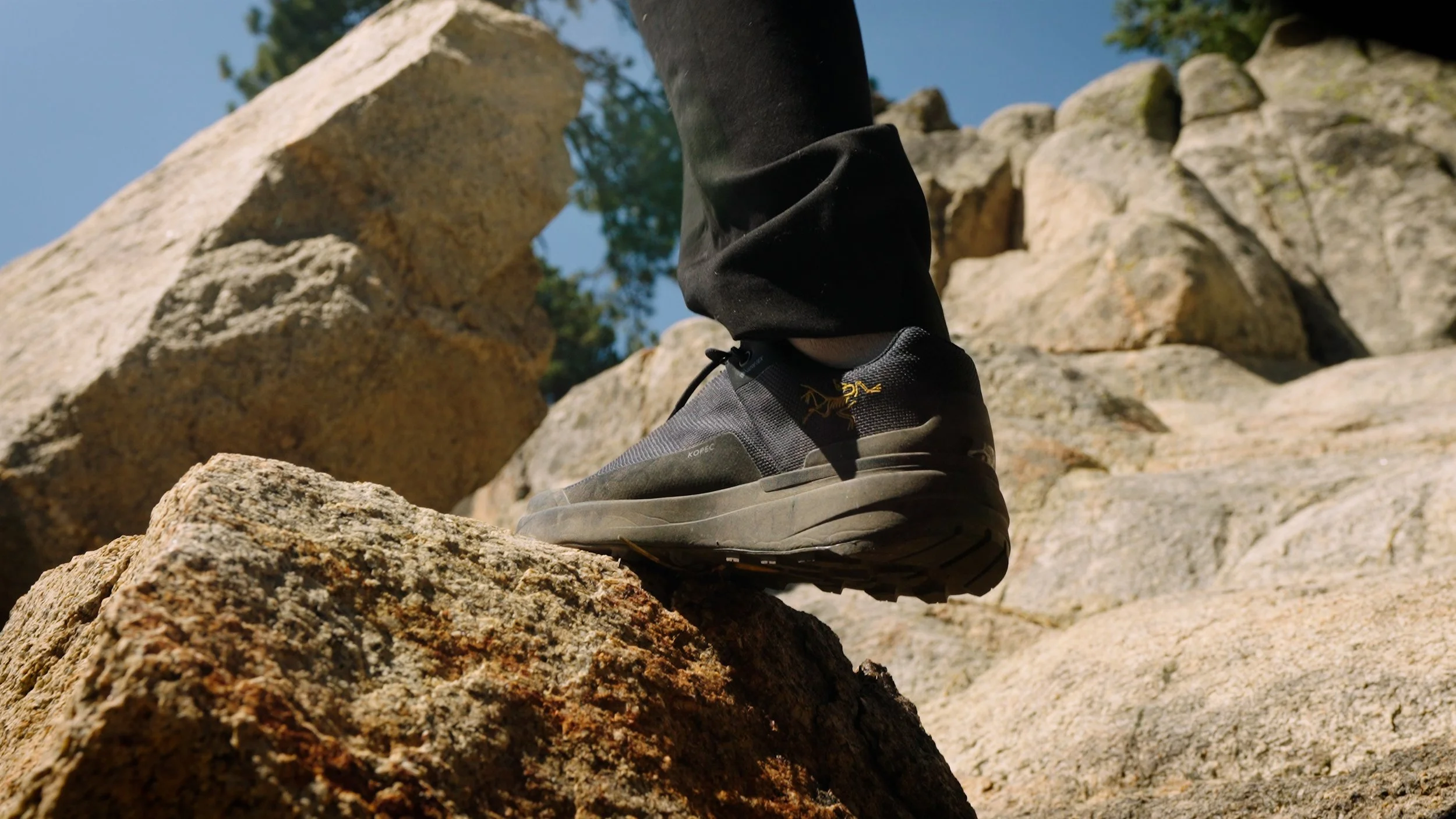 Close-up of a person's foot wearing a black and gray hiking shoe climbing over rocks outdoors.