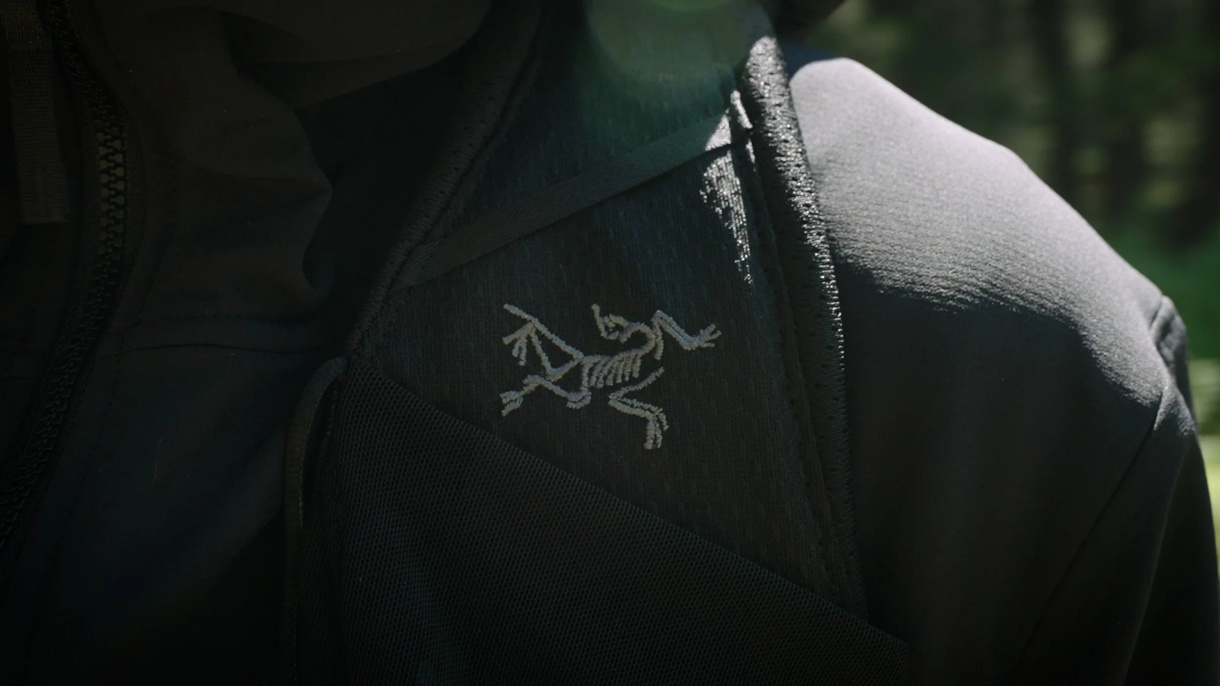 Close-up of a black jacket with a chess knight embroidered on the chest pocket, worn by someone outdoors.