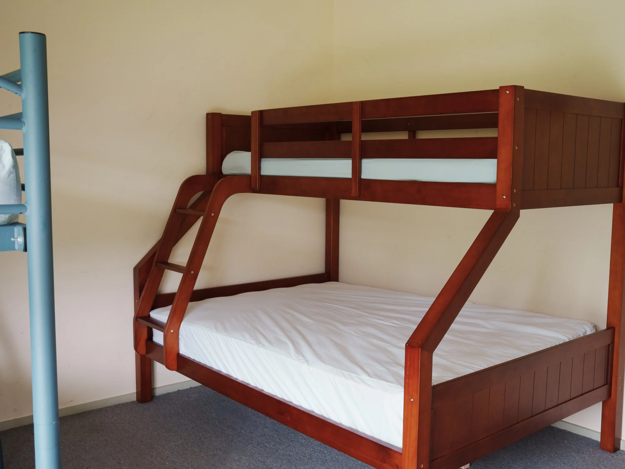 Wooden bunk bed with white mattresses against a beige wall.