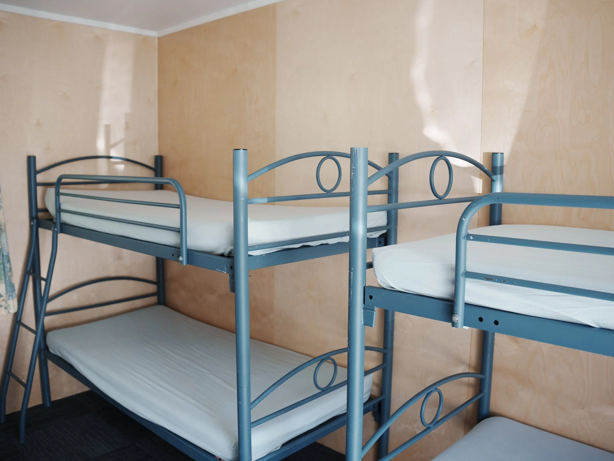 Blue metal bunk beds with white mattresses in a beige-walled room.