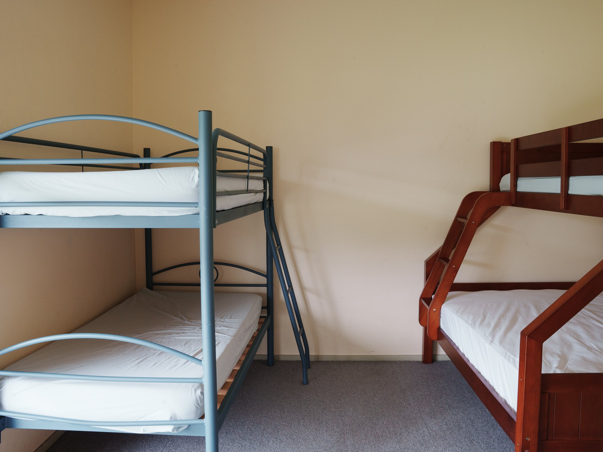 A room with two sets of bunk beds, one metal and one wooden, against beige walls.