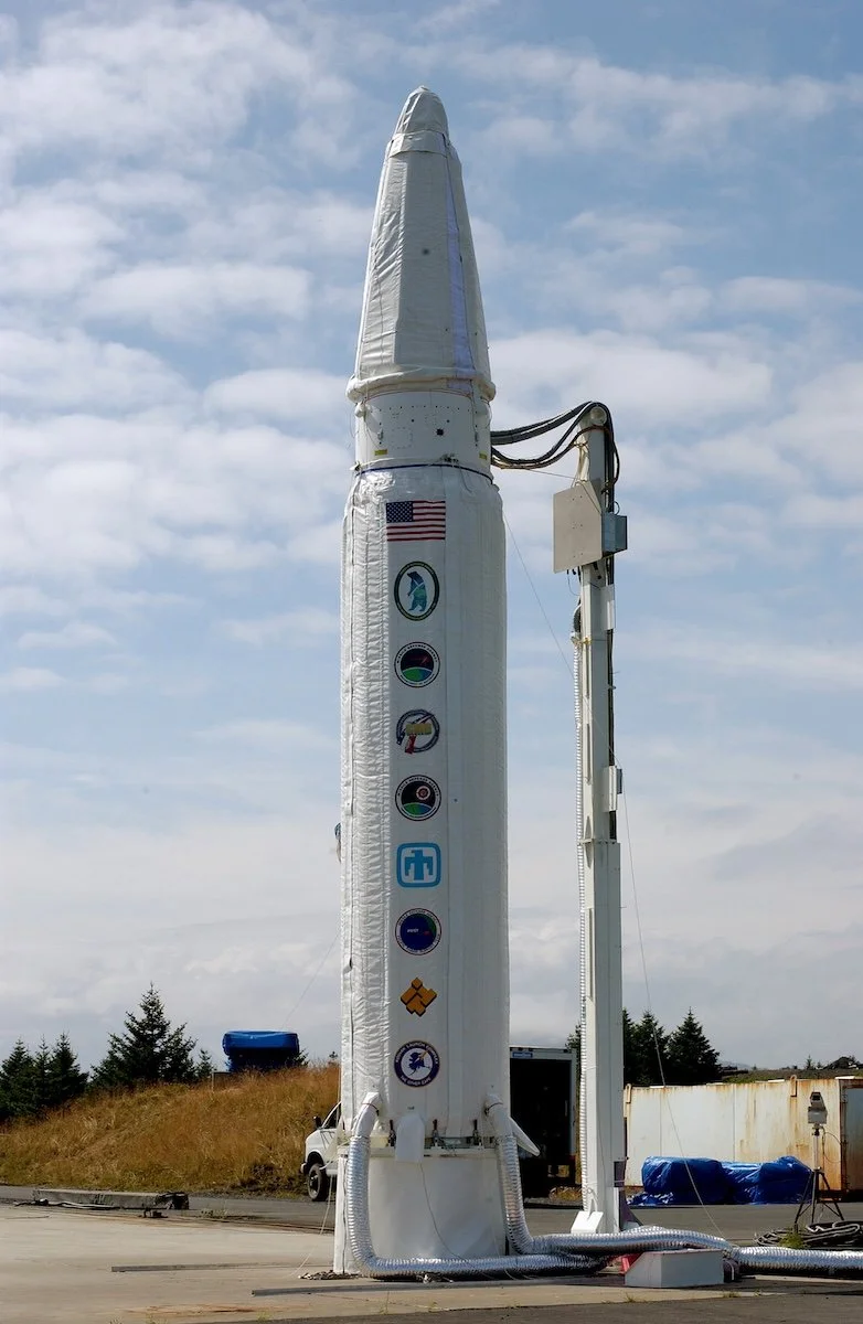 A rocket test stand with various NASA and SpaceX logos on the side, located outdoors under a partly cloudy sky.