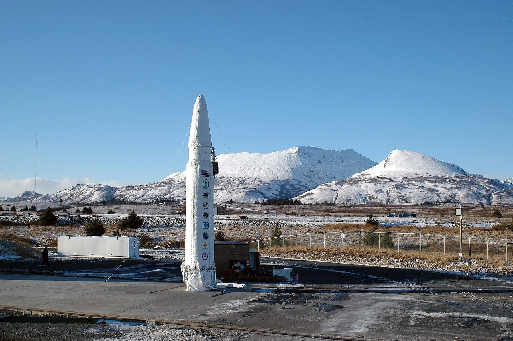 A rocket standing on a launch pad in a snowy landscape with mountains in the background under a clear blue sky.