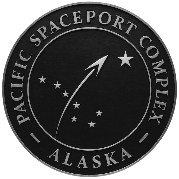 Black circular patch with silver border and text reading "Pacific Spaceport Complex Alaska." The center features a silver rocket leaving a trail through a constellation of stars.
