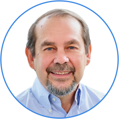 A middle-aged man with gray hair and a beard, smiling, wearing a light blue collared shirt, against a white background with a blue circular border.