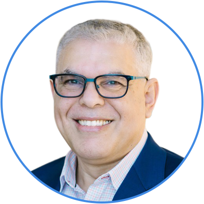 Portrait of a man with short gray hair, glasses, smiling, wearing a dark suit jacket and a light-colored collared shirt, against a white background with a blue circular border.