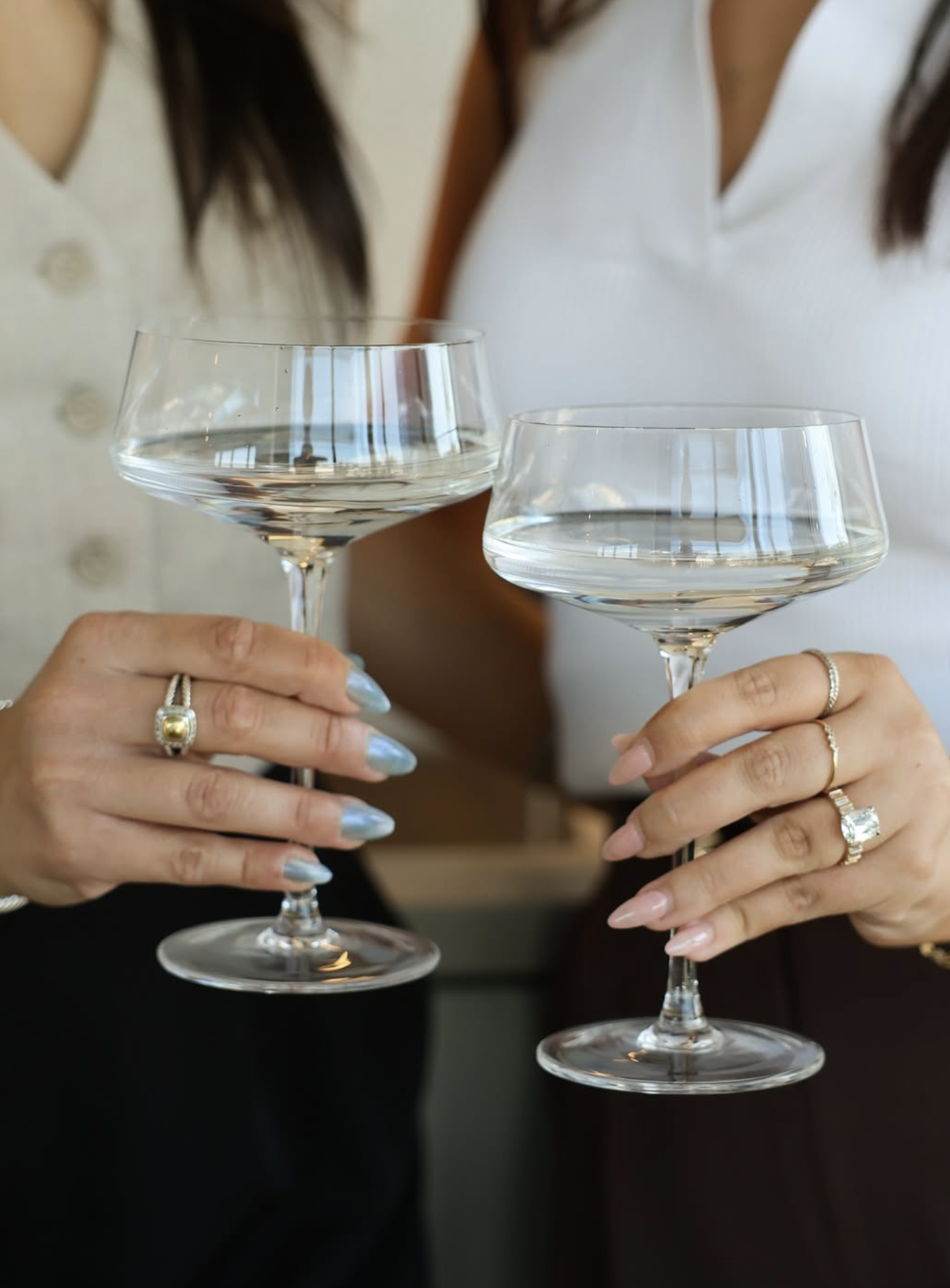 Two manicured hands holding cocktail glasses as a toast to the camera