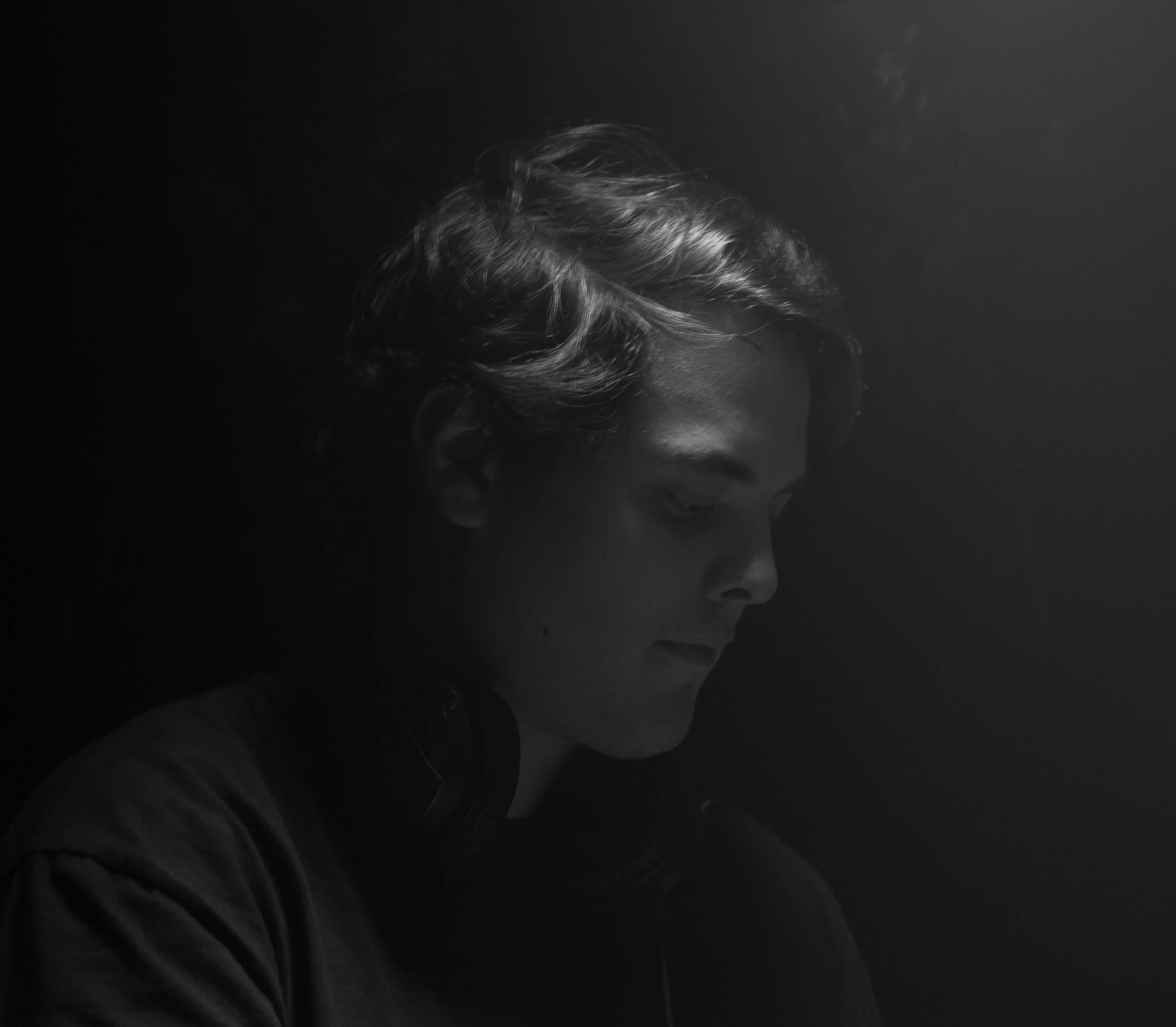 Joven con auriculares mirando hacia abajo en un entorno oscuro.