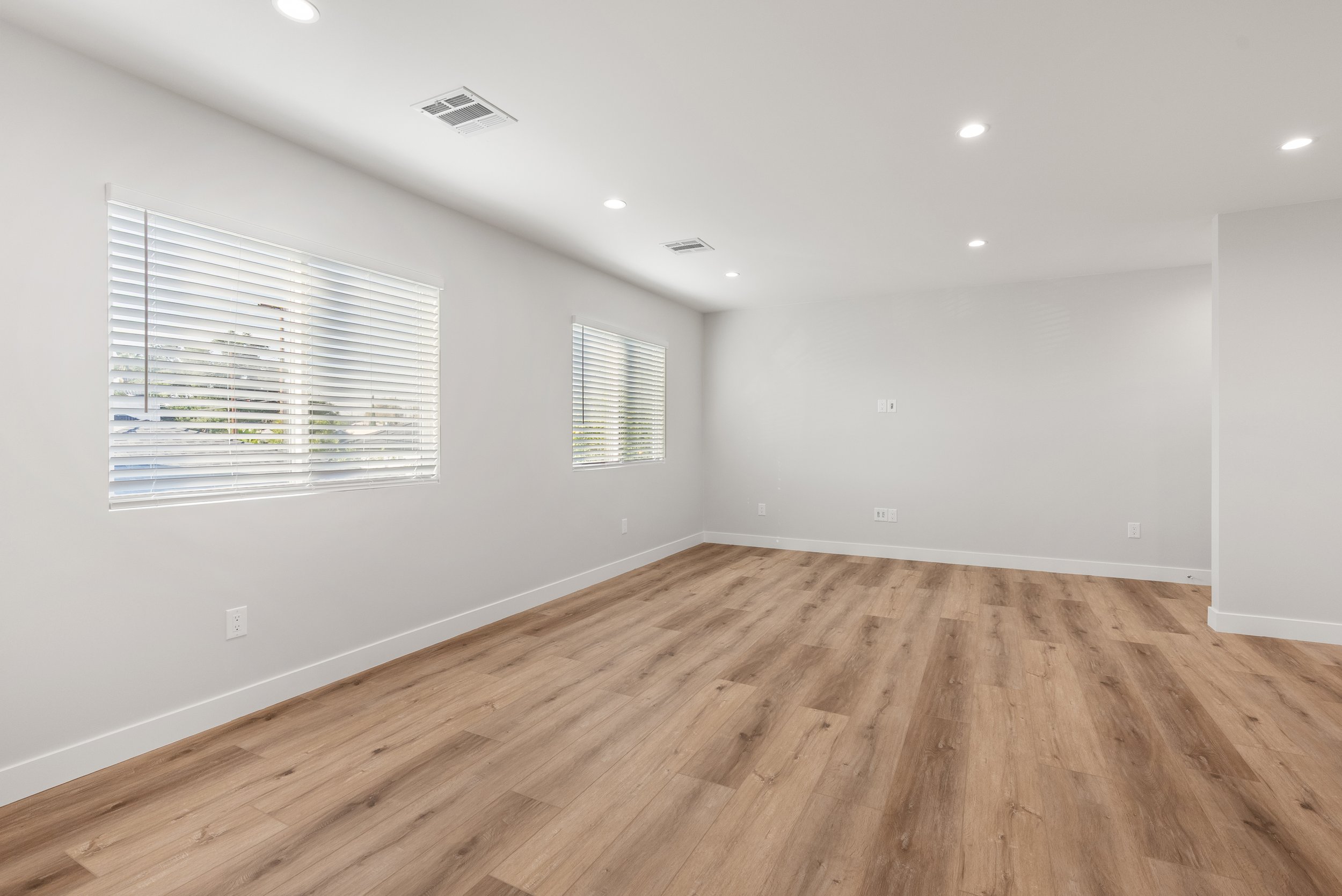 Empty room with hardwood floors, white walls, two windows with blinds, and ceiling lights.