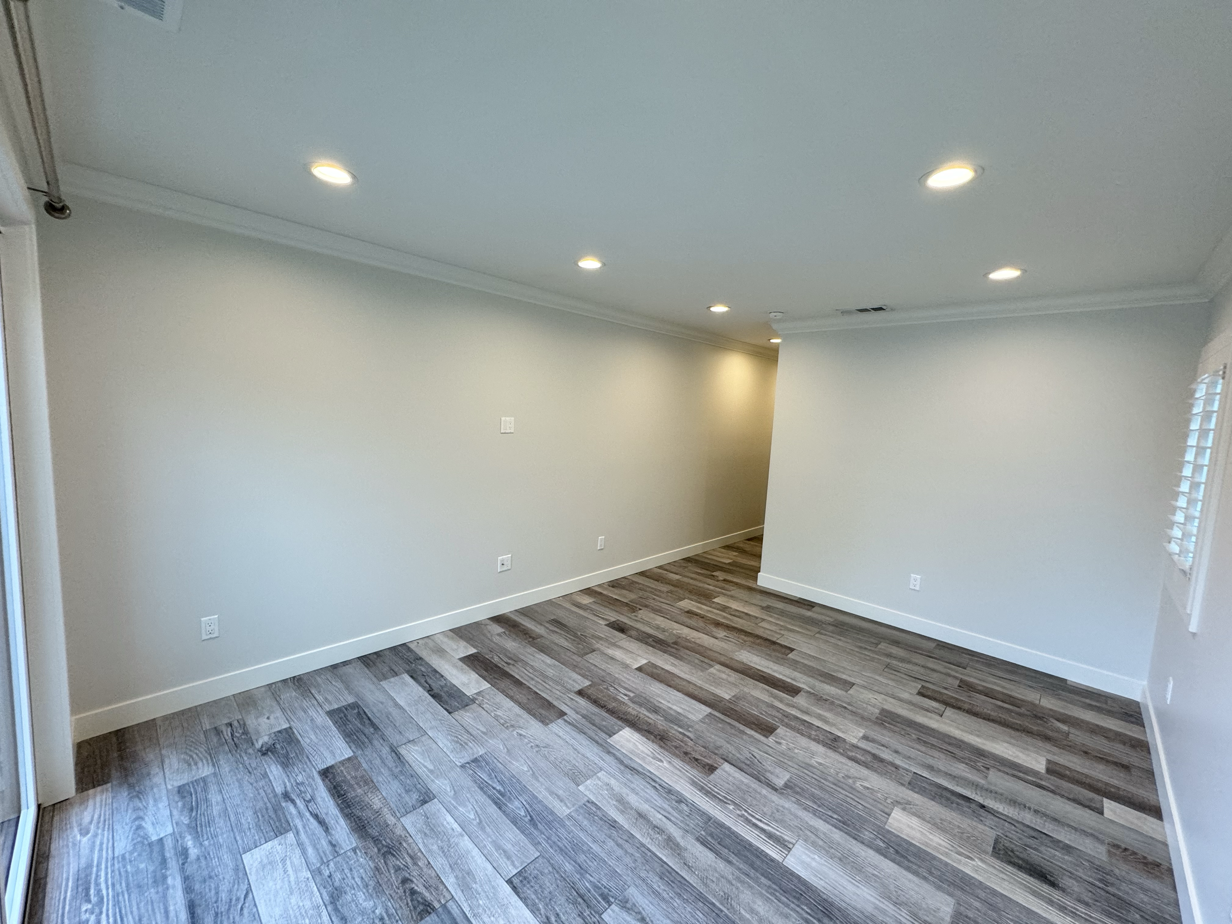 Empty room with light-colored walls, hardwood flooring, and ceiling recessed lighting, with a window on the right side.