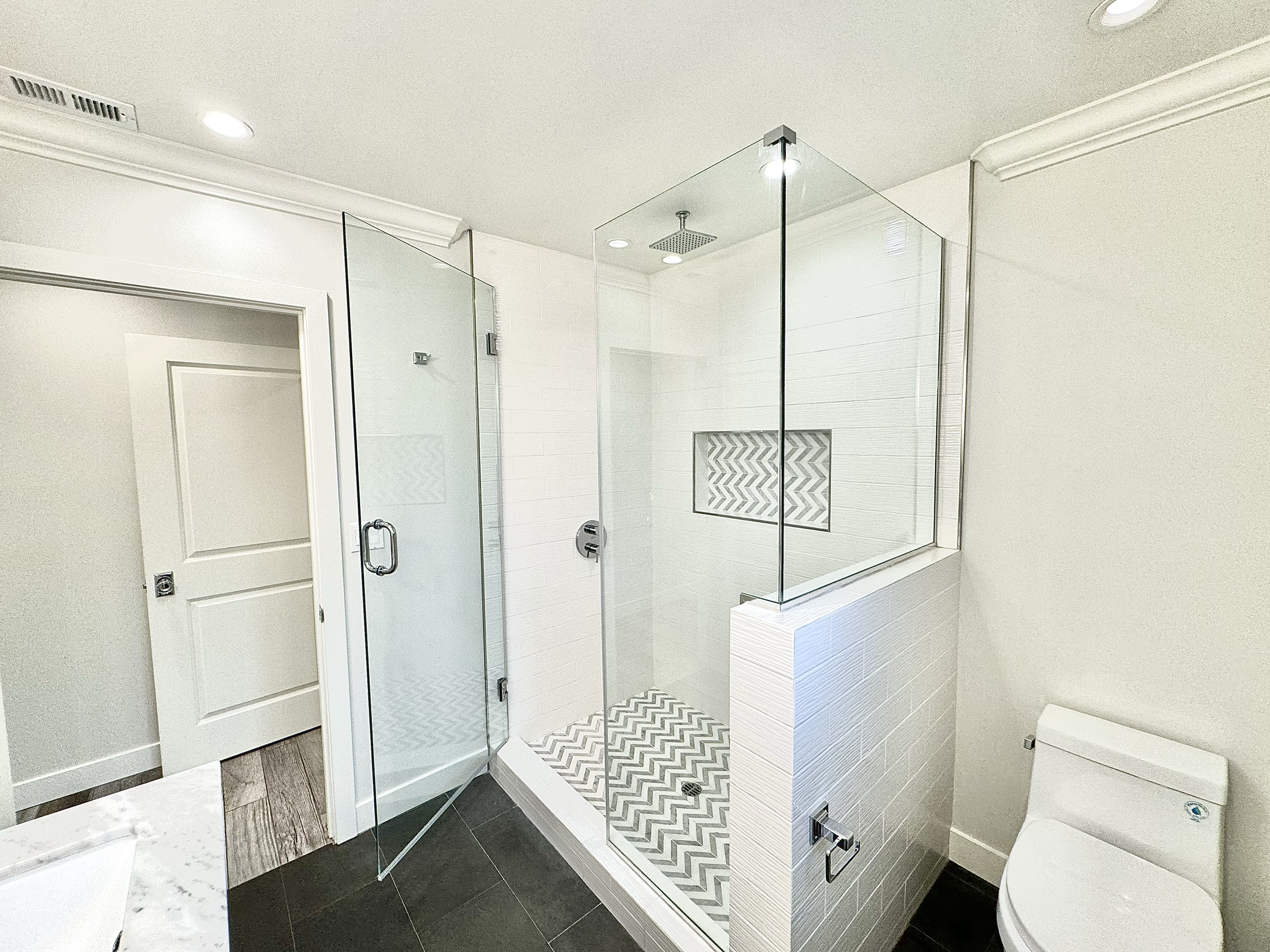 Modern bathroom with glass-enclosed walk-in shower featuring gray herringbone tiles and white wall tiles, with a built-in niche, and a white toilet.