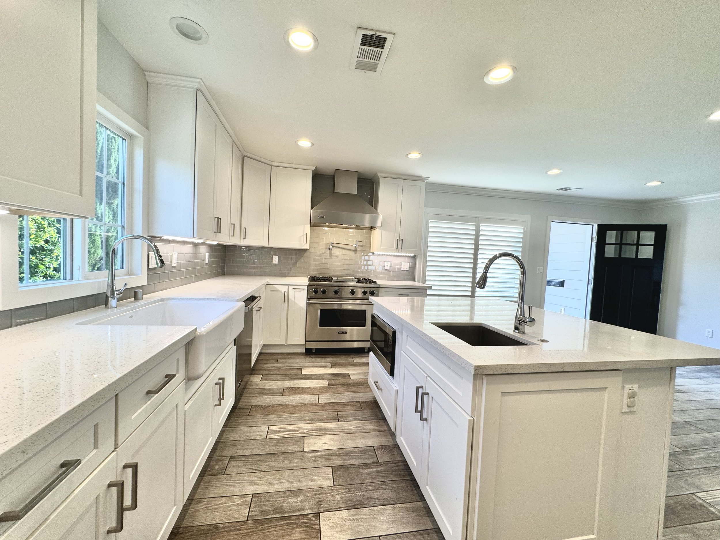 Modern kitchen with white cabinets, stainless steel appliances, gray backsplash, white countertop, window, and wooden flooring.