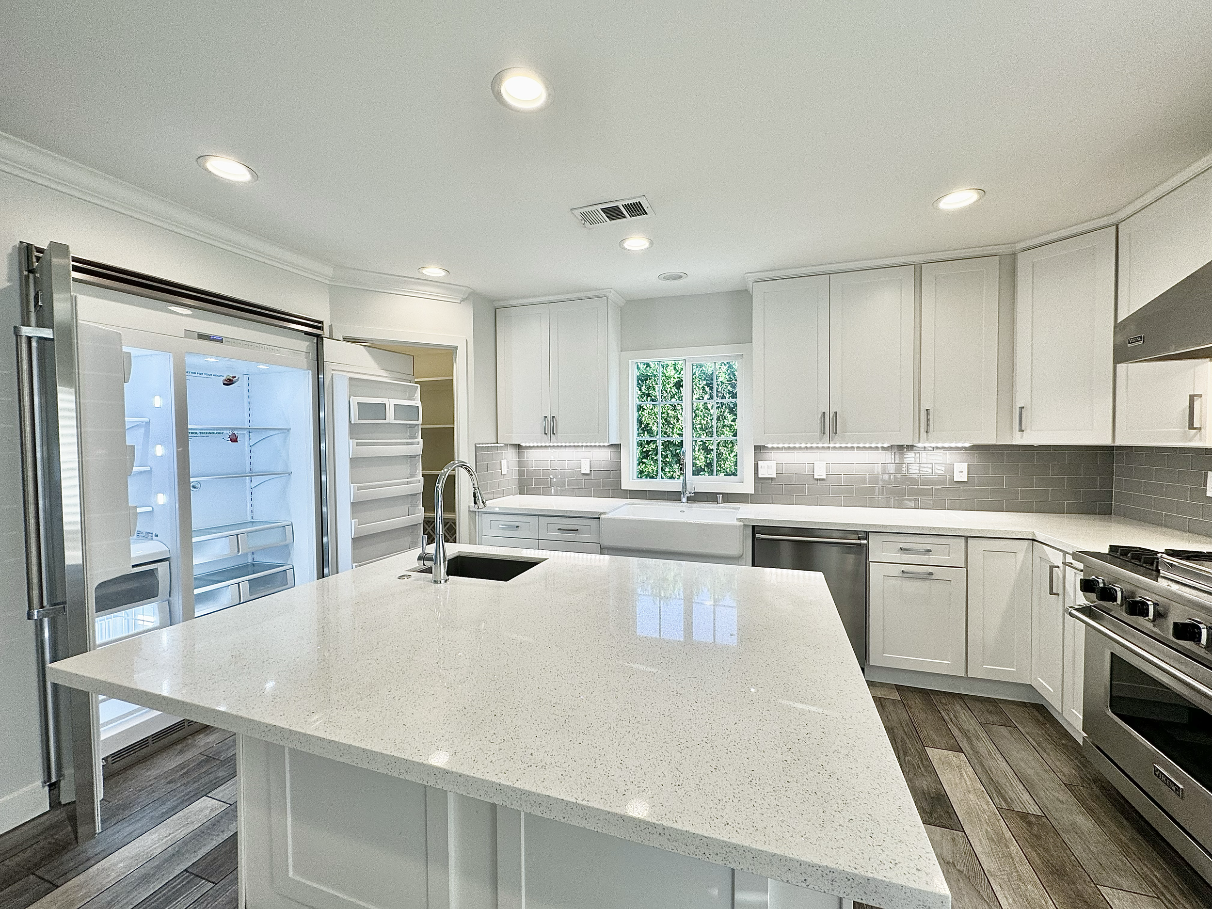 Modern kitchen with white cabinets, gray tile backsplash, stainless steel appliances, and a large white island counter.