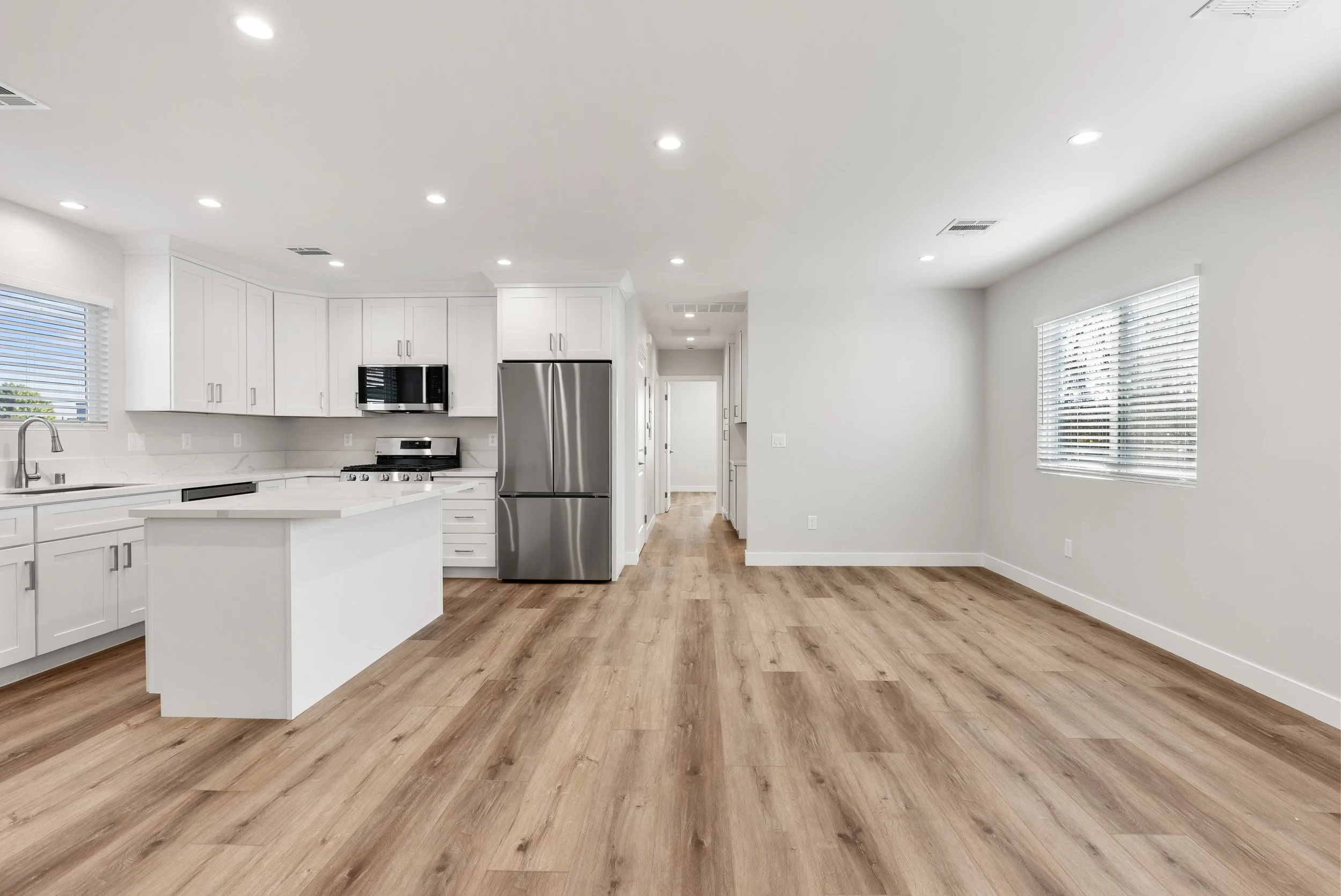 Empty modern kitchen and dining area with white cabinets, stainless steel appliances, and light wood flooring.