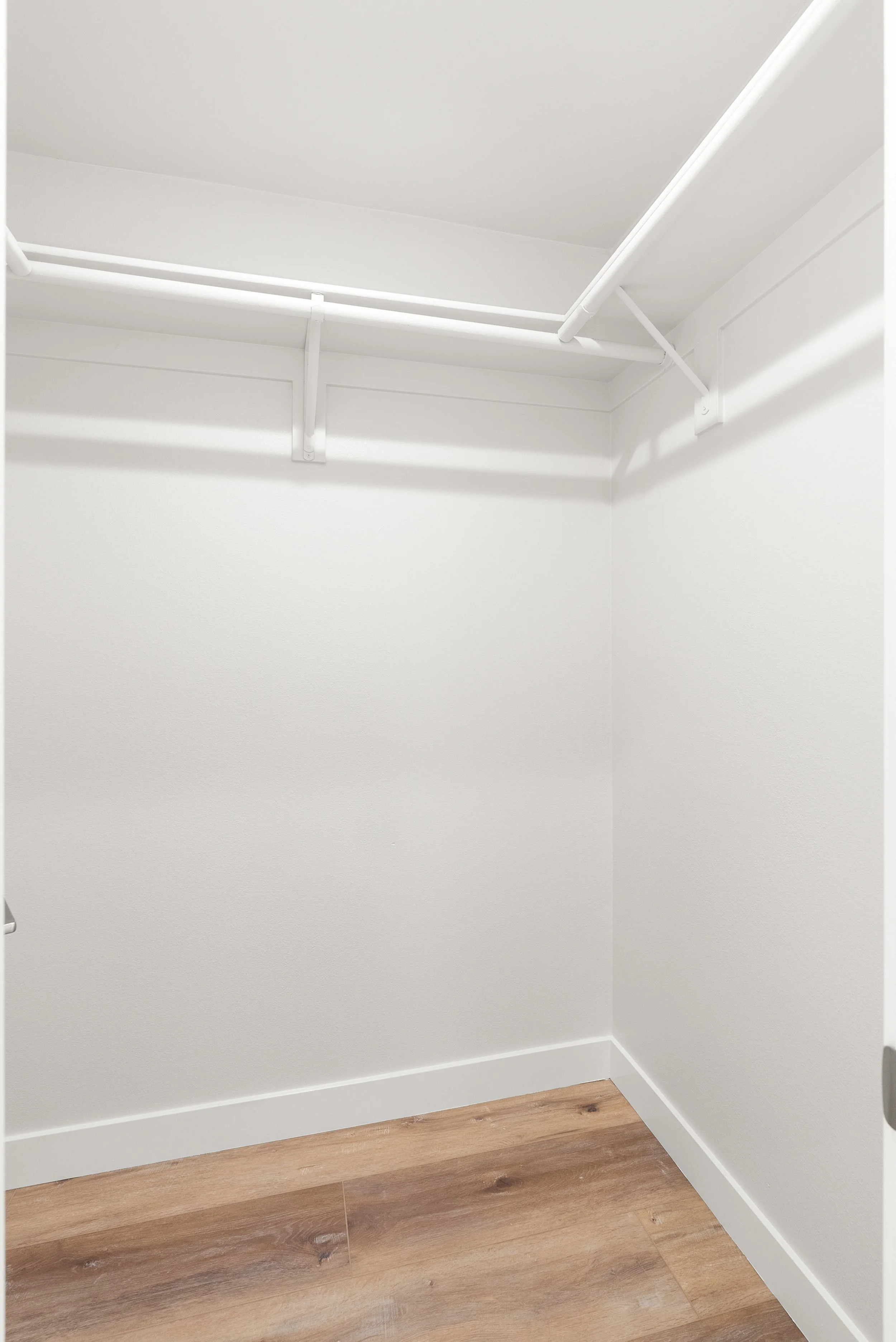 Empty walk-in closet with white walls, ceiling, and shelving, and a wooden floor.