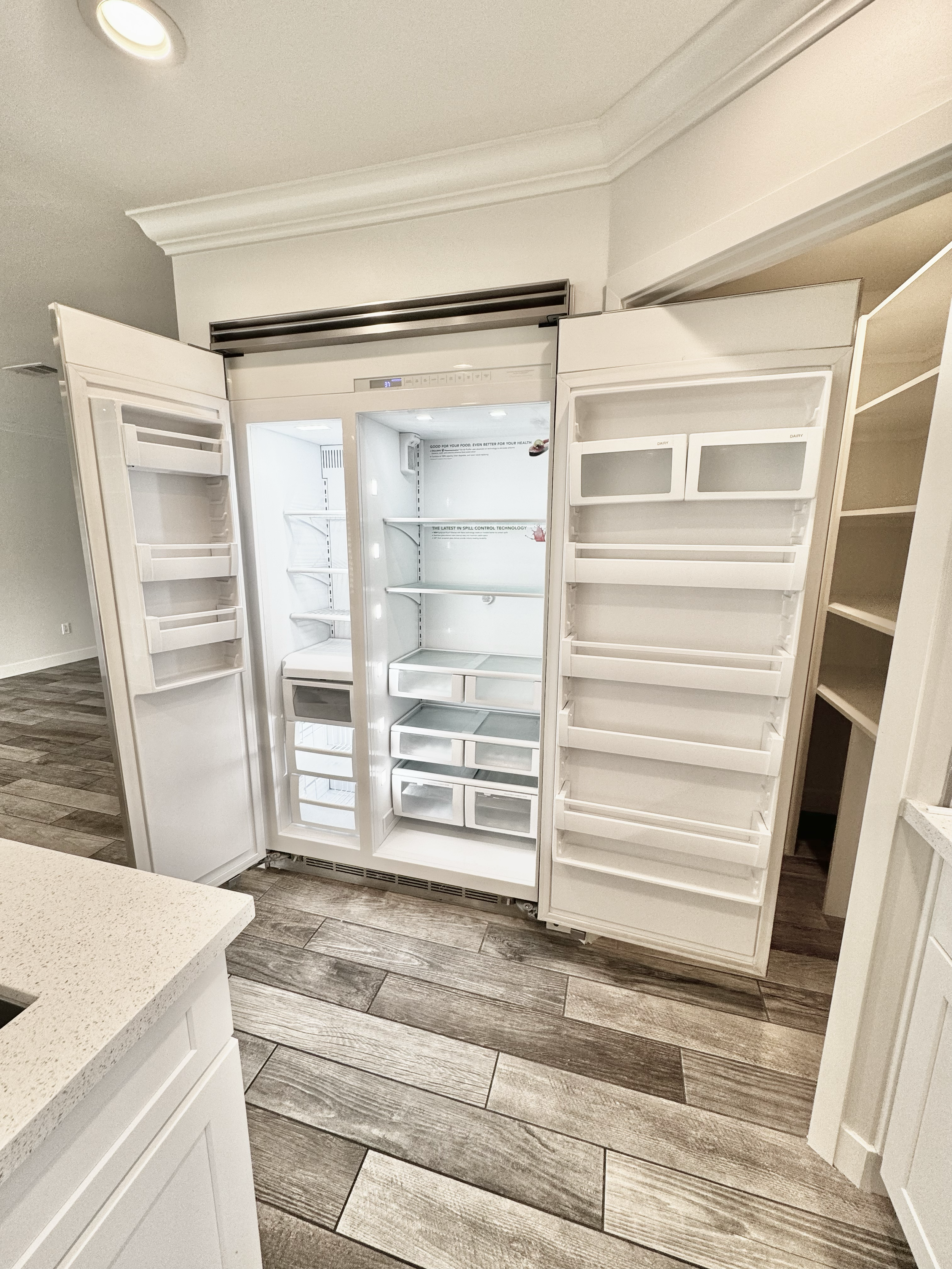 Open empty white refrigerator with shelves and drawers in a kitchen with wooden floor.