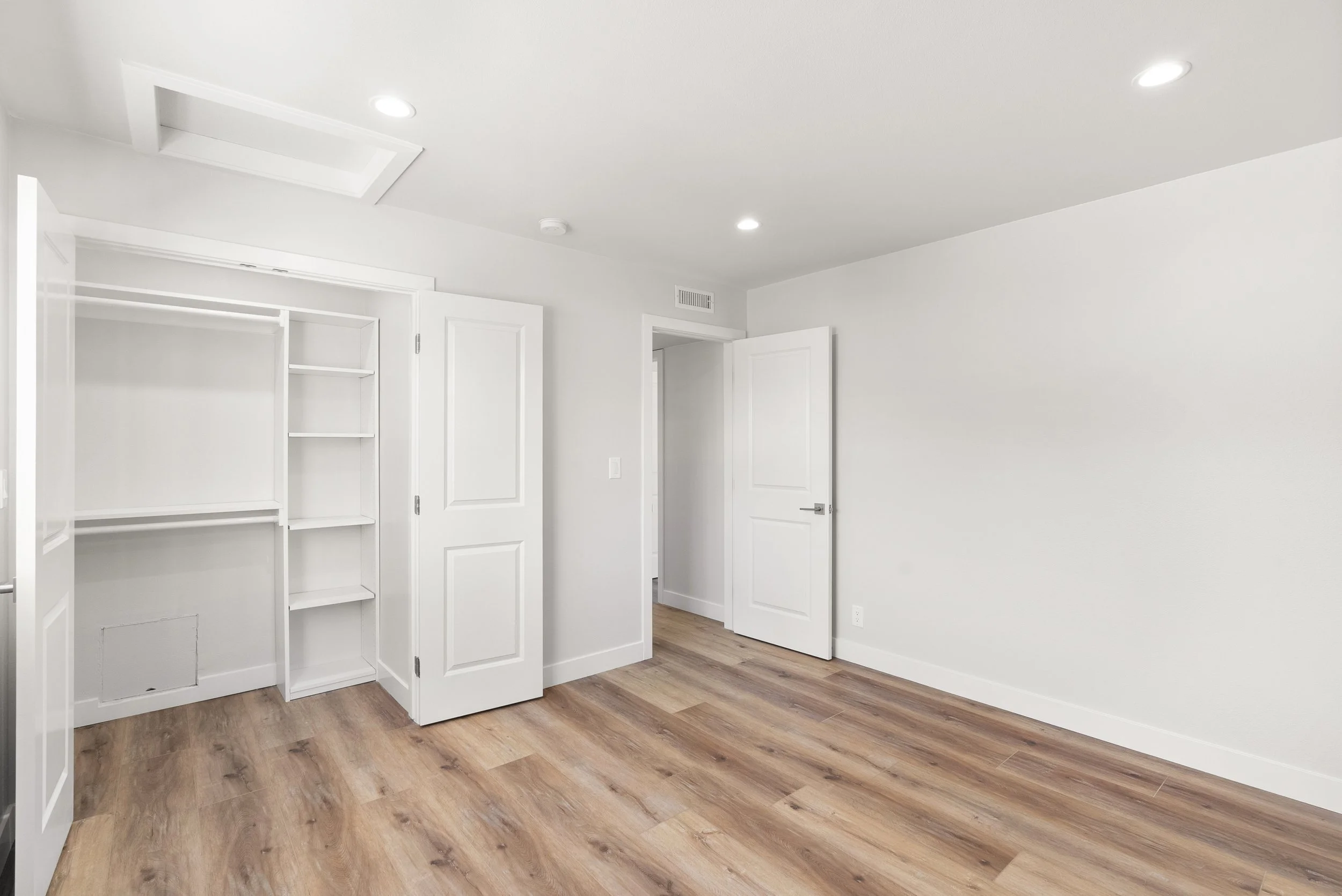 Empty room with white walls, hardwood floors, open closet with shelves, and two closed doors.