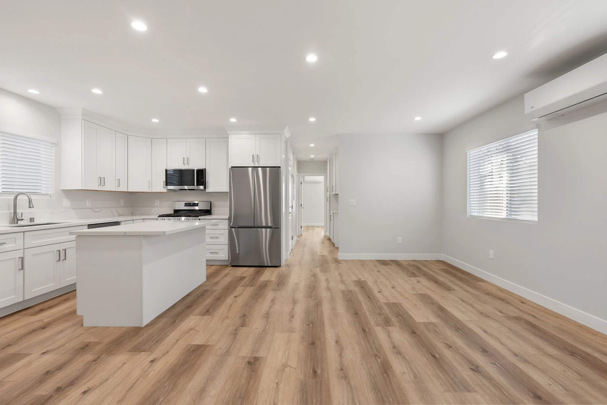 Empty modern kitchen with white cabinets, stainless steel appliances, and hardwood floors.