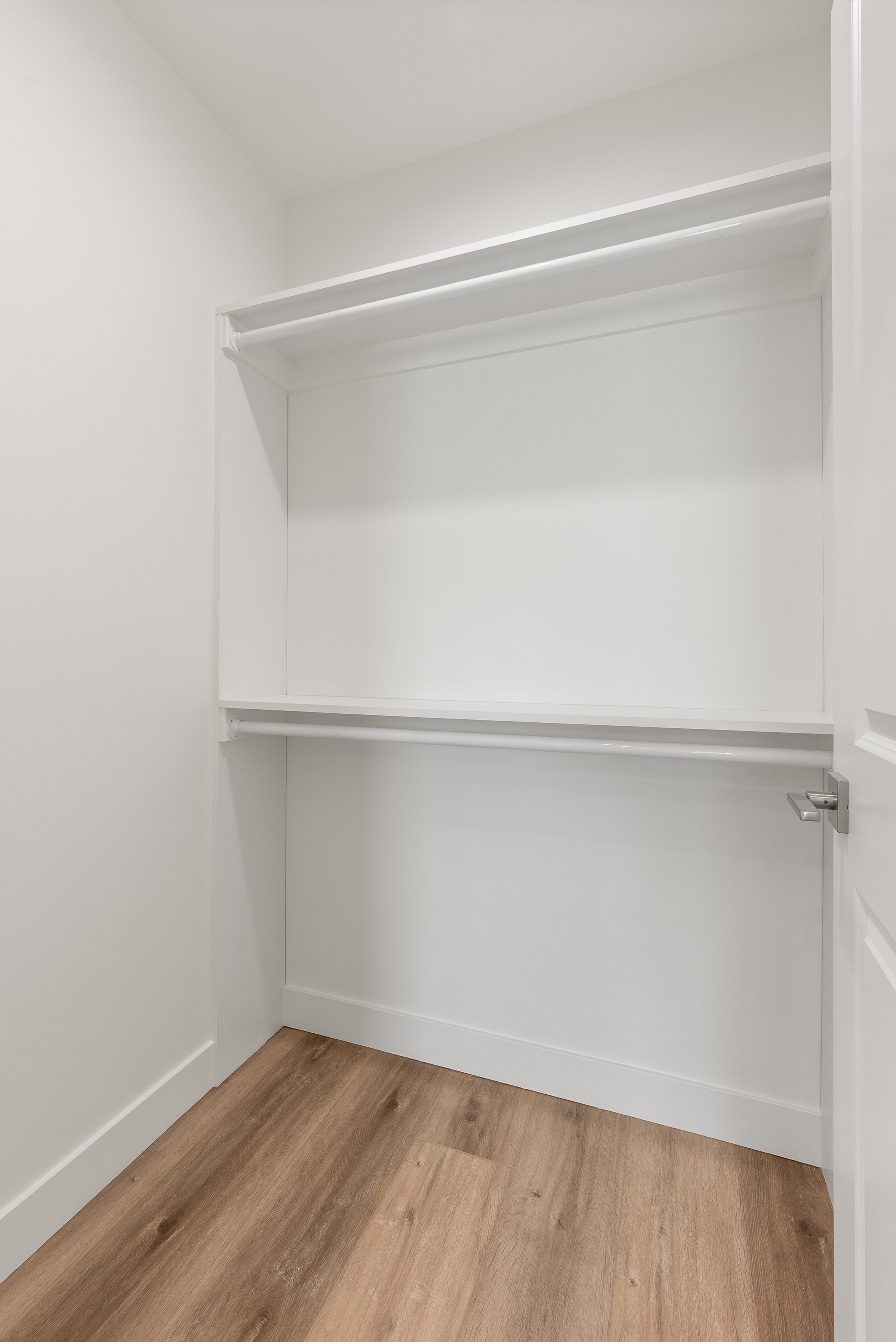 Empty white closet with two shelves and a rod for hanging clothes, with wood flooring.