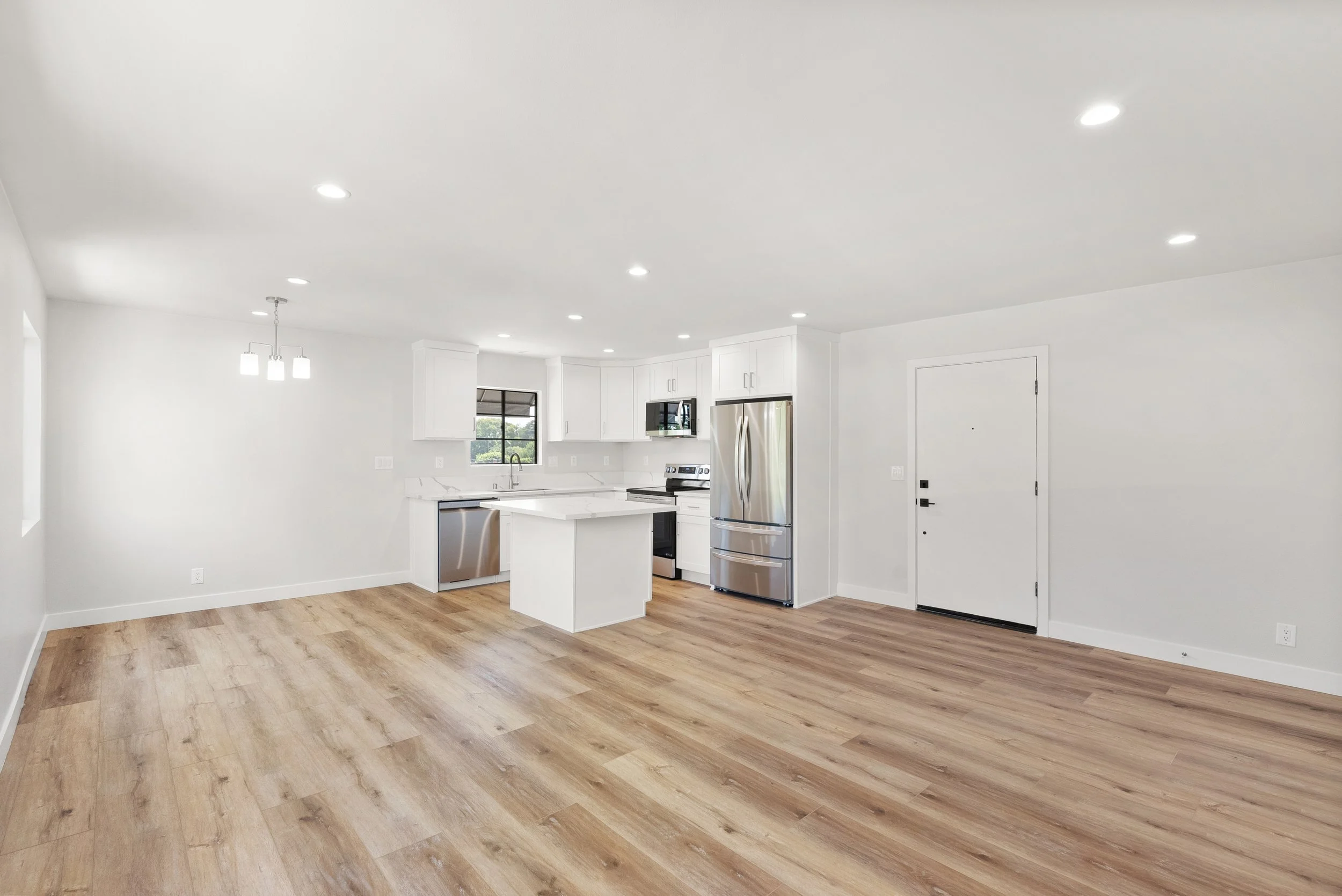 Empty modern kitchen with white cabinets, stainless steel appliances, hardwood floors, and a small island, in an open living space.