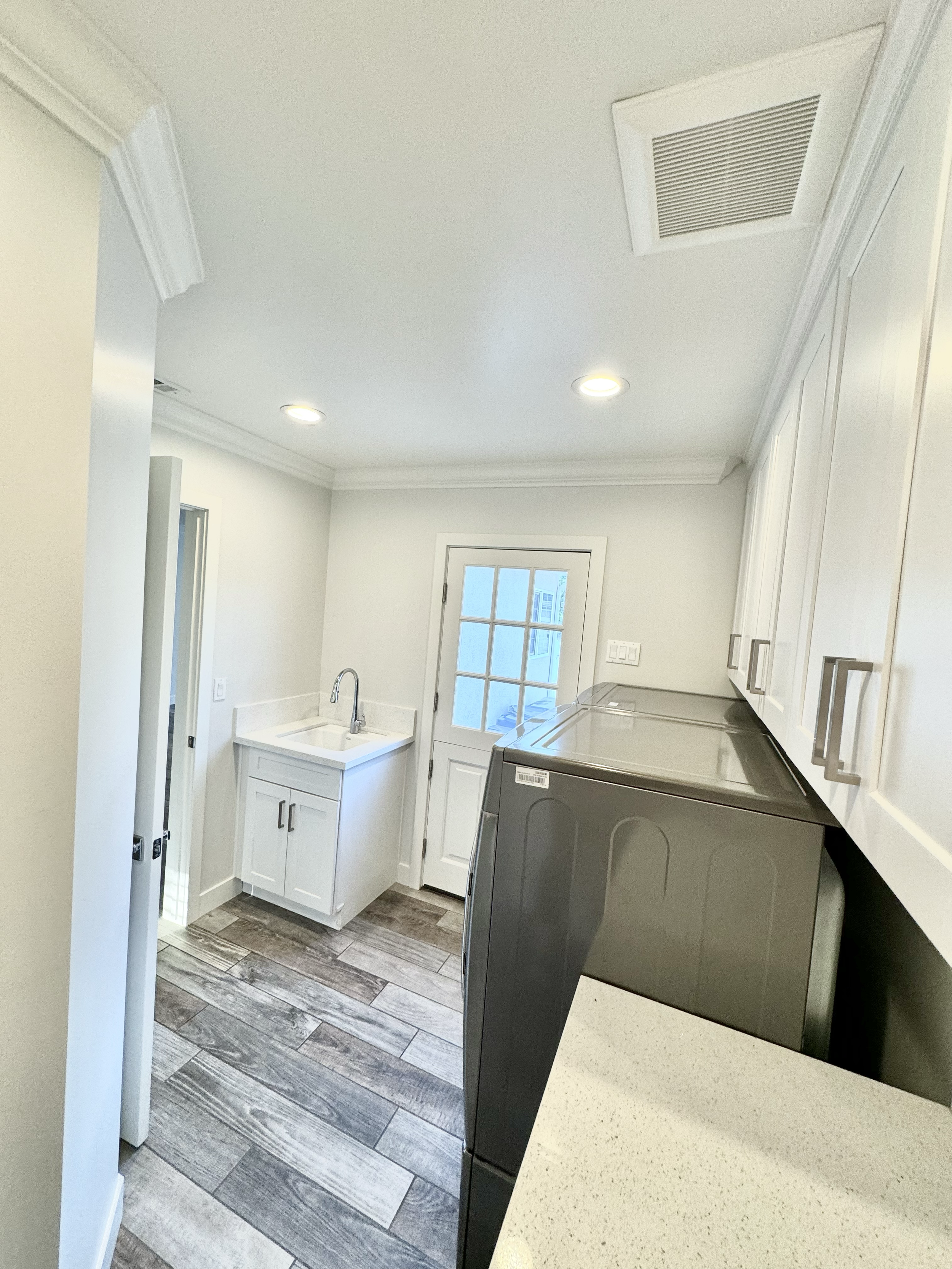 Clean laundry room with white cabinets, a stainless steel washing machine, a small sink, and a door with glass panels leading outside.