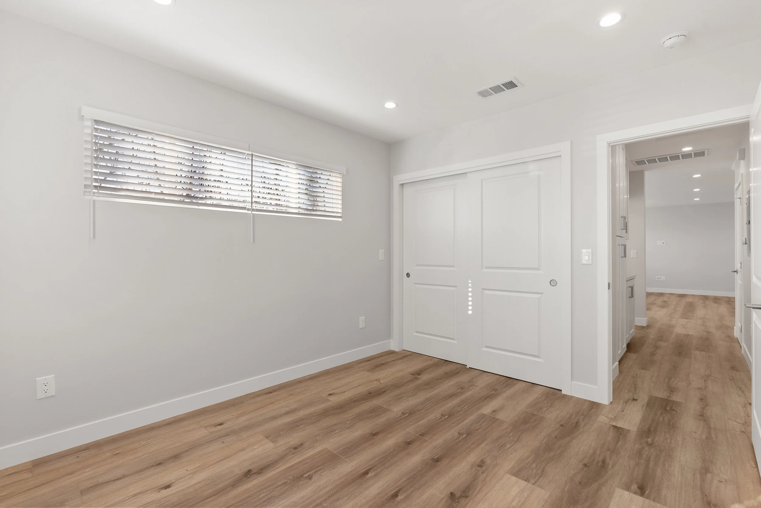 Empty room with white walls, a window with blinds, and hardwood flooring.