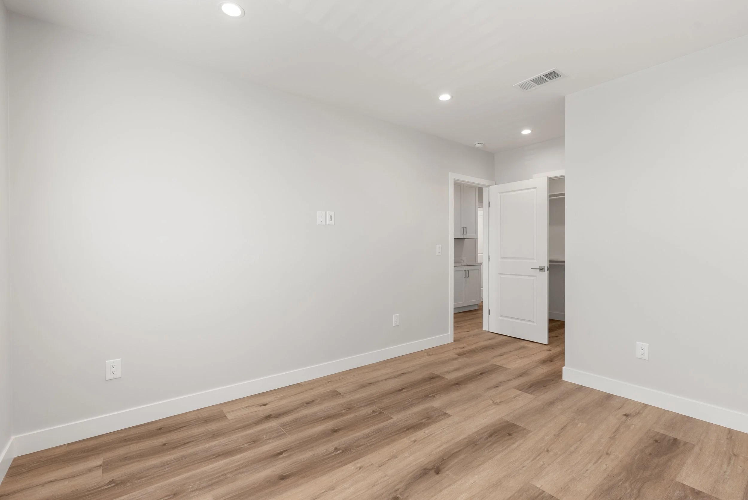 Empty room with white walls, wood flooring, and a door leading to a closet and a bathroom.