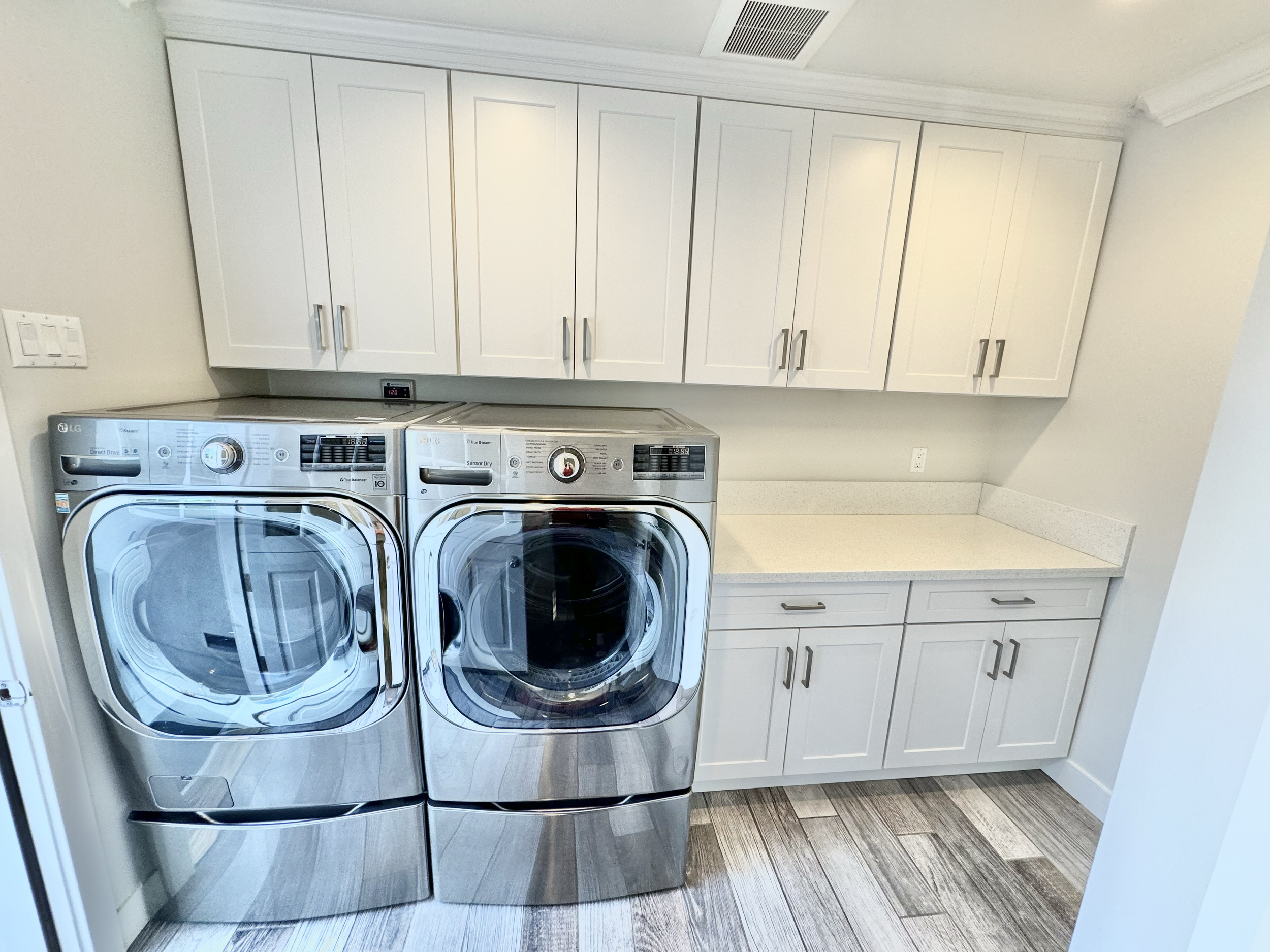 Laundry room with white cabinetry, a stainless steel washer and dryer, and laminate flooring.