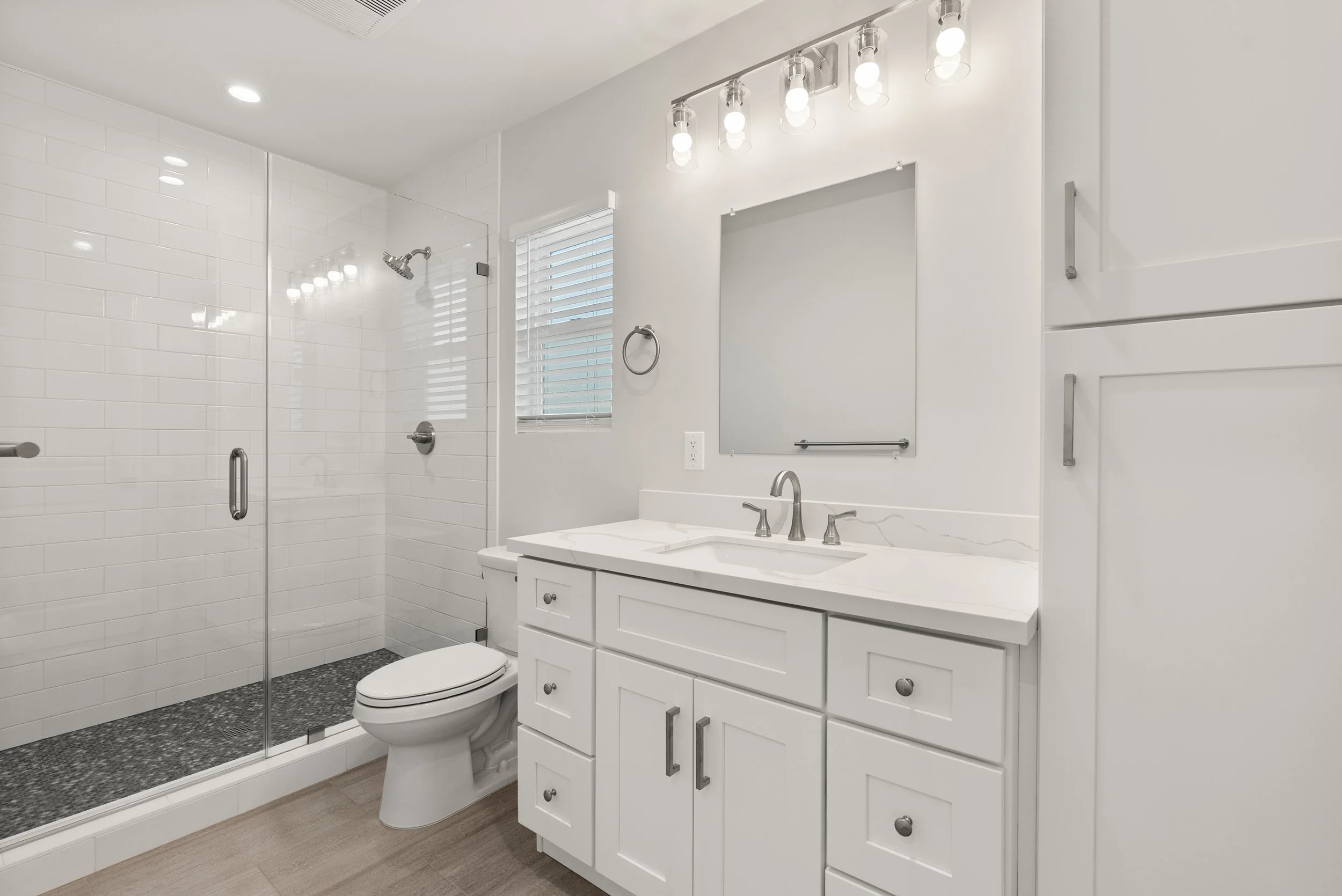 A modern bathroom with a glass shower, white cabinetry, a white sink, and a mirror.