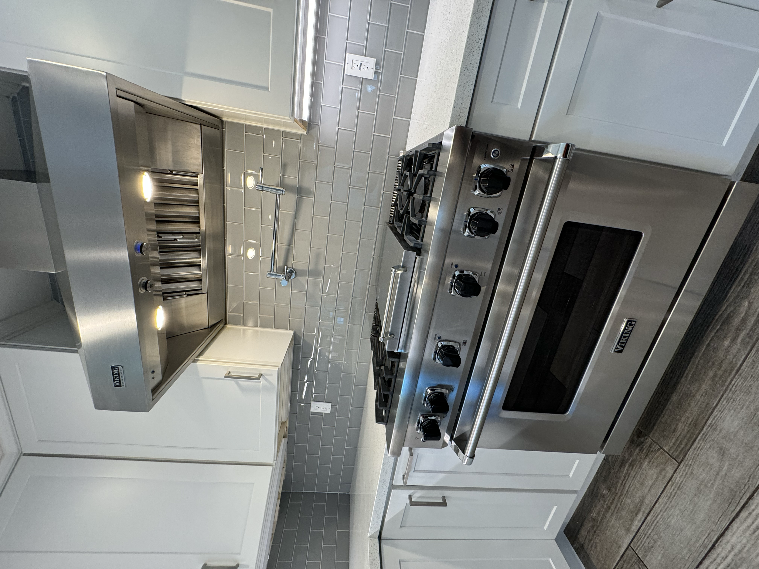 Stainless steel kitchen stove with four burners and black control knobs, against a light gray backsplash with gray grout tiles, and white cabinetry.