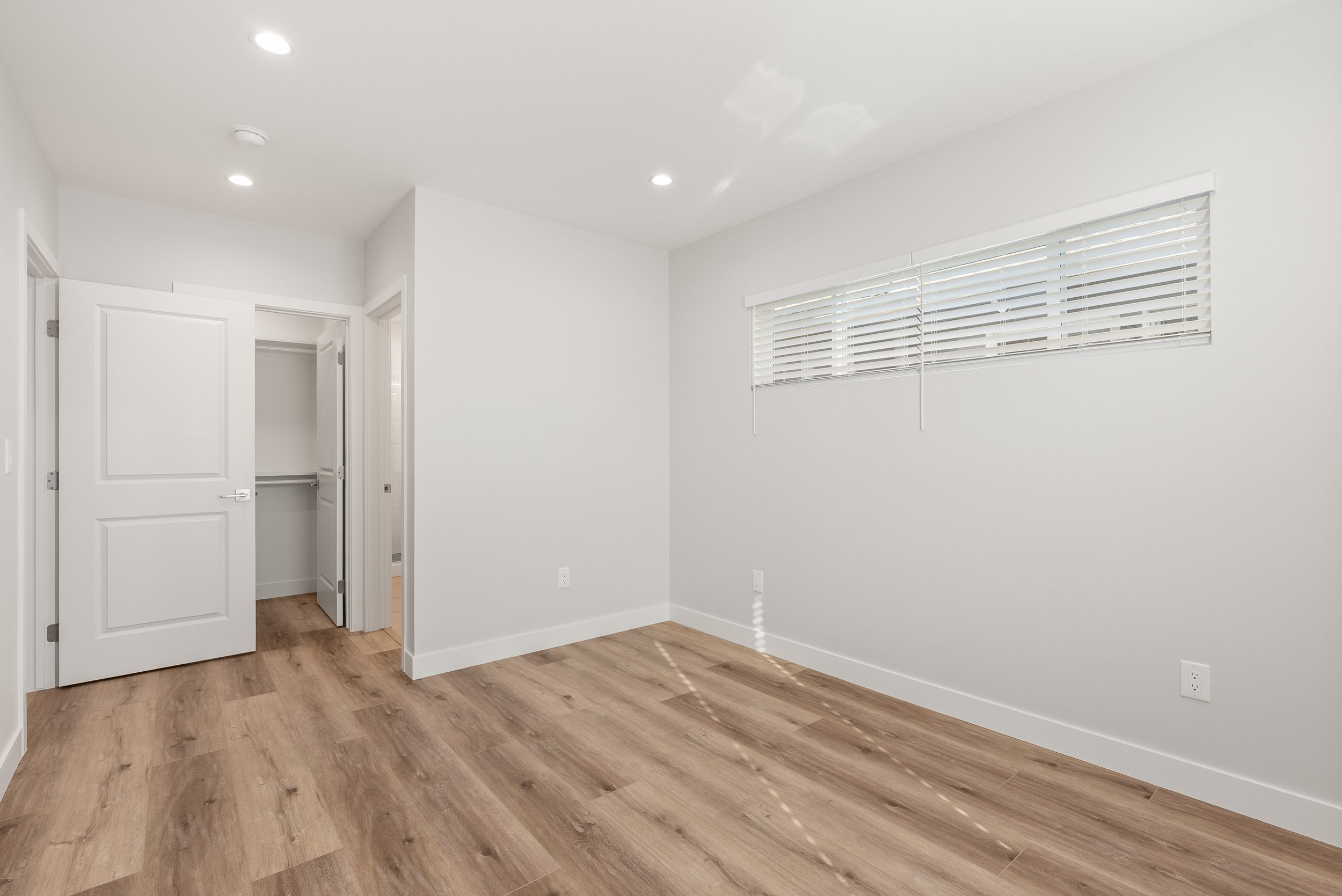 Empty room with white walls, wood flooring, window with white blinds, and open closet door.