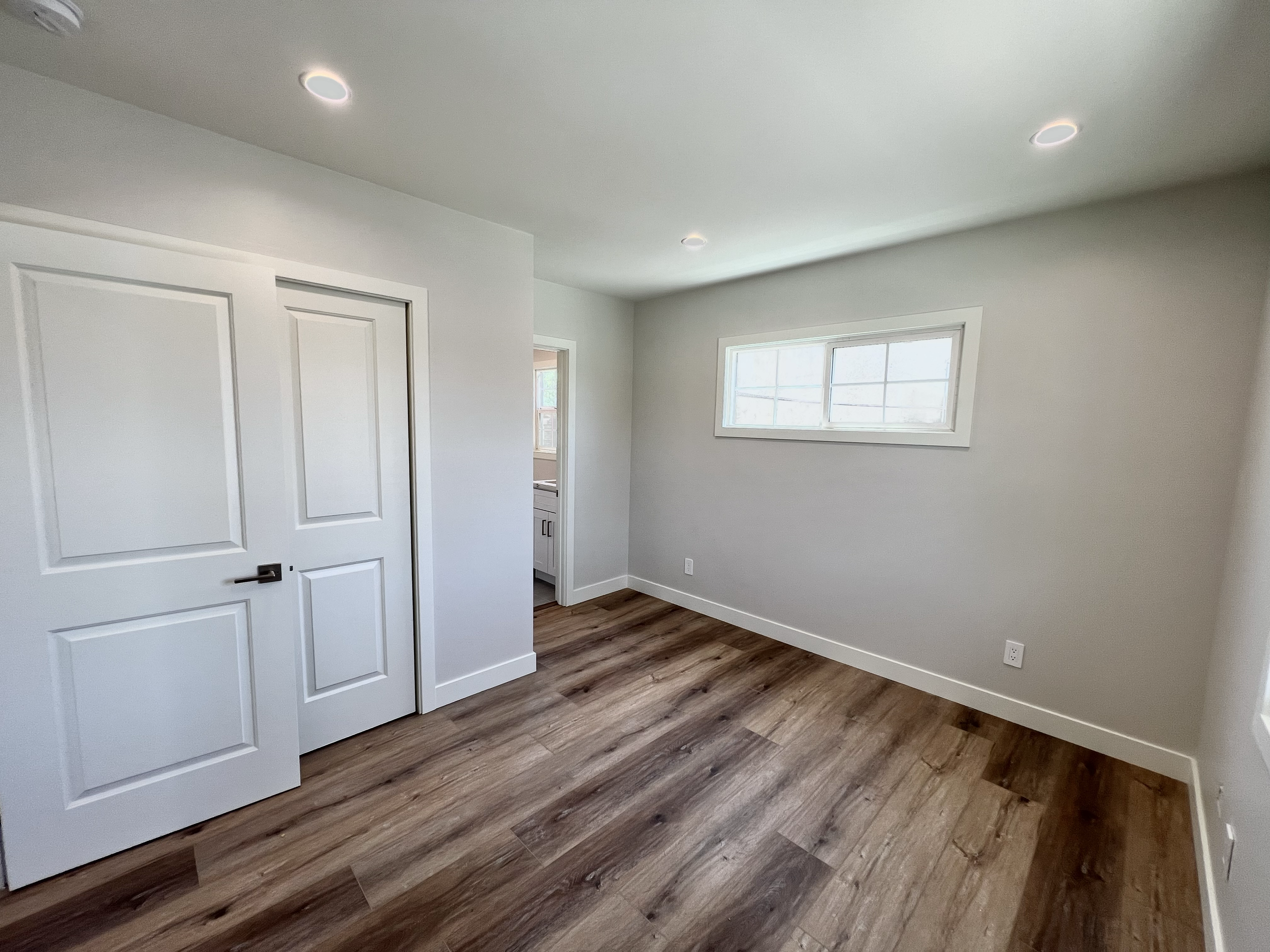 Empty room with white walls and wood laminate flooring, a window on the right wall, and a closed double closet door on the left.