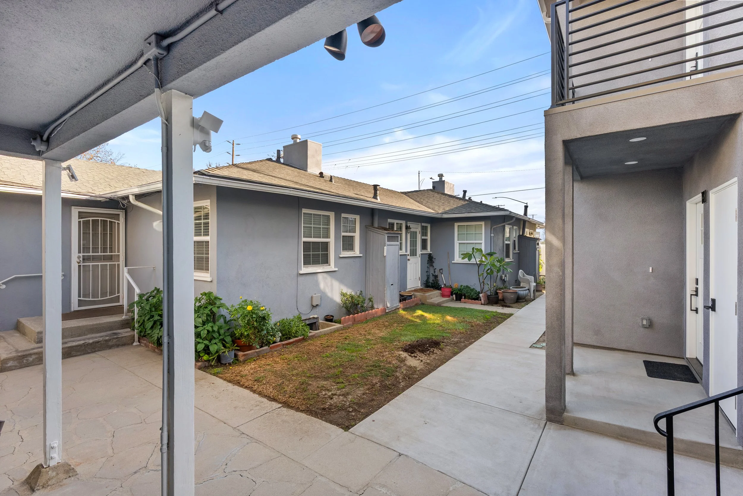 View of a small courtyard between residential buildings with plants and a patch of grass, under a blue sky.