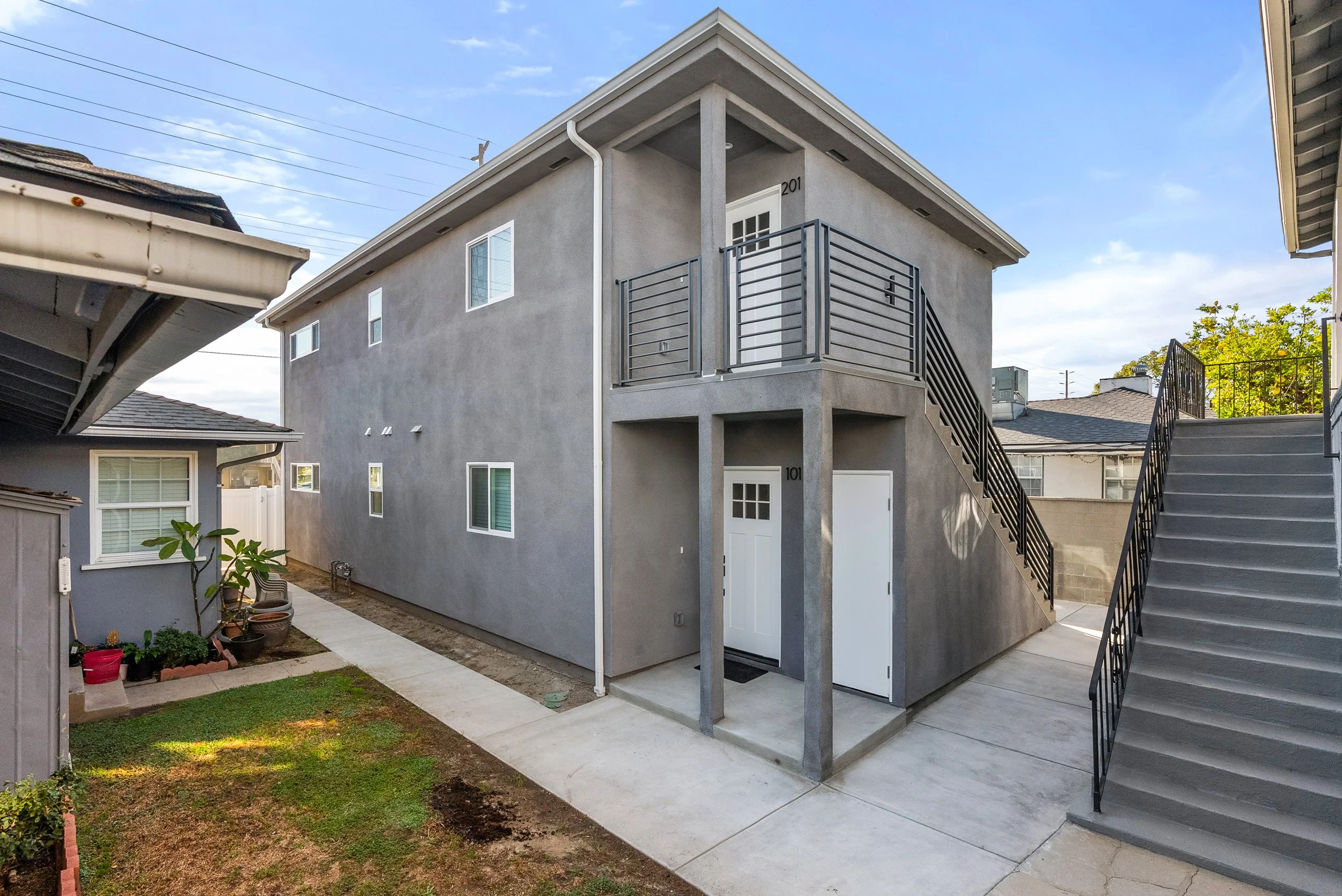Rear view of a modern two-story apartment building with gray exterior, including doors and staircases, under a blue sky.