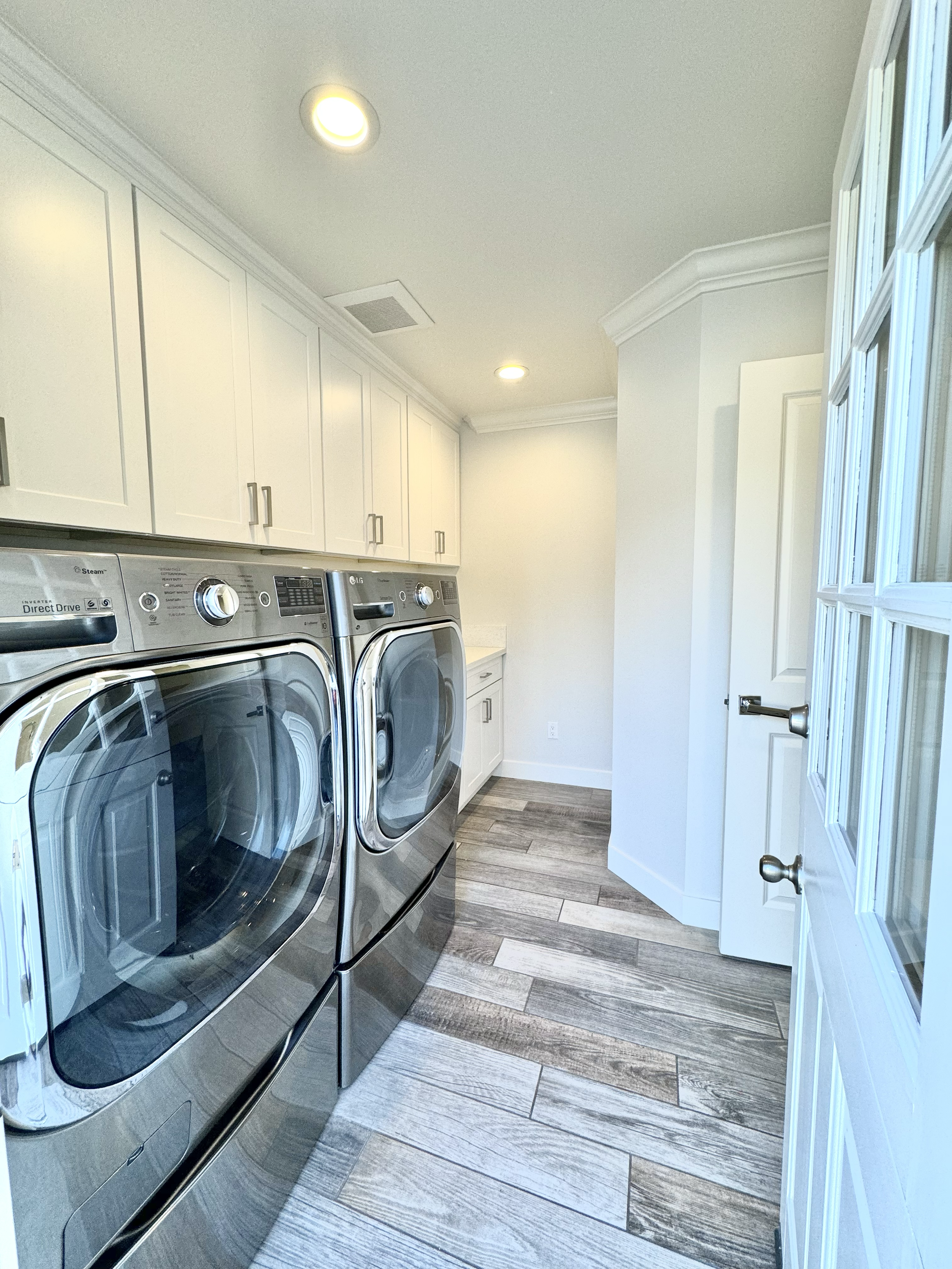 Laundry room with front-loading washer and dryer, white cabinets, and wooden floor.